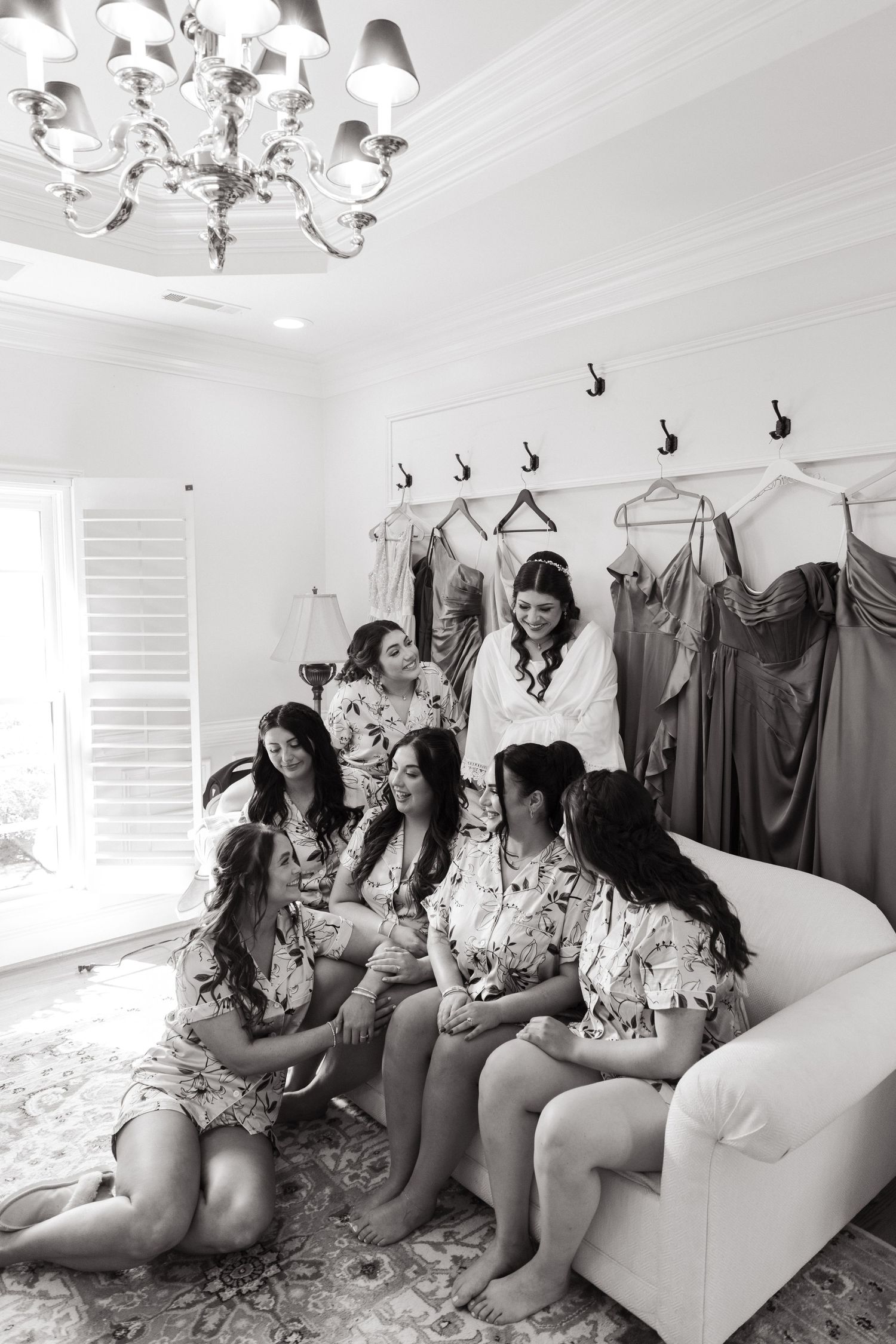Group enjoying time together on a white couch in a dressing room with formal gowns hanging on the wall.