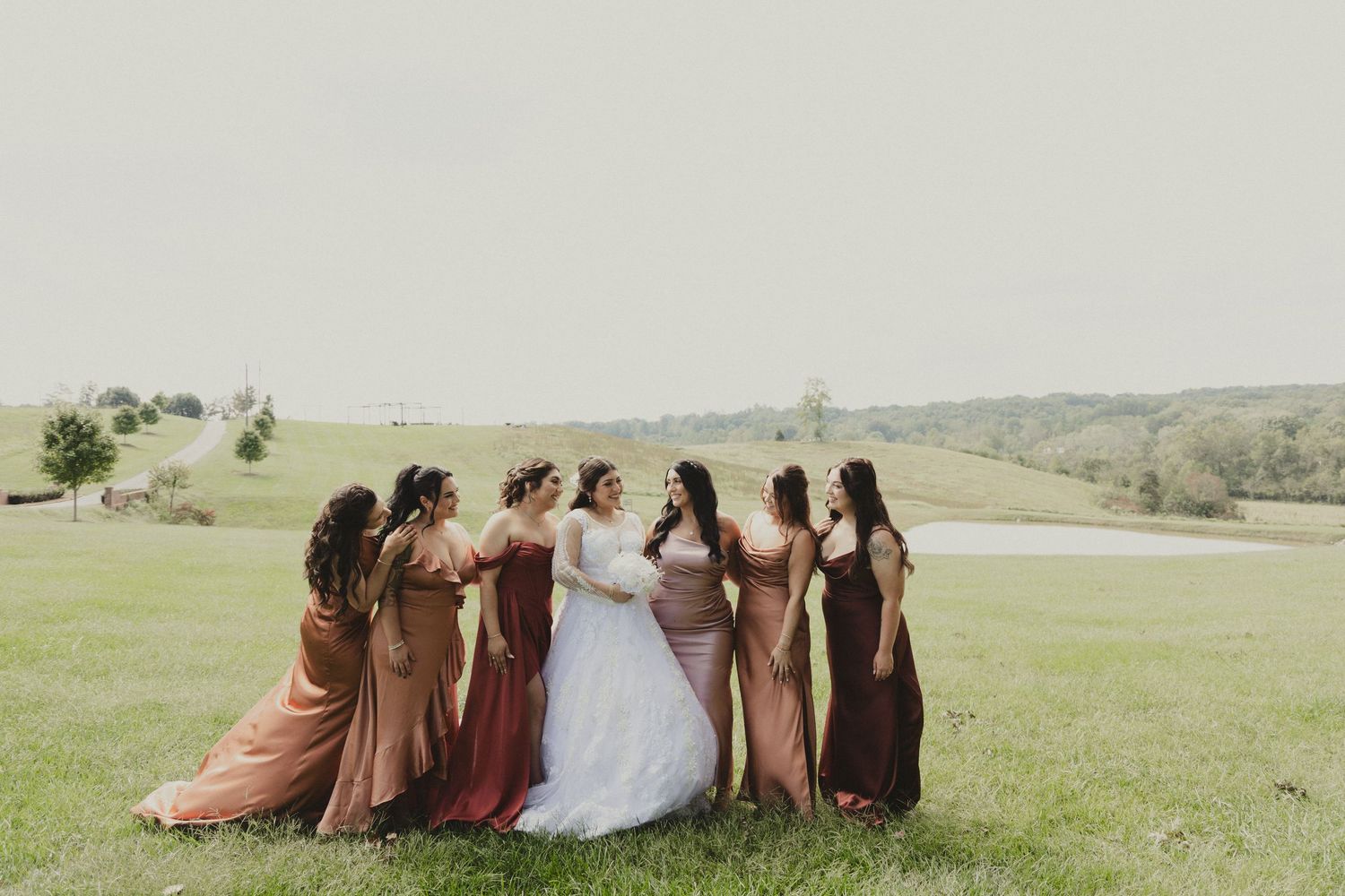 A group in formal dresses stand together on a grassy hilltop for a special outdoor event celebration.