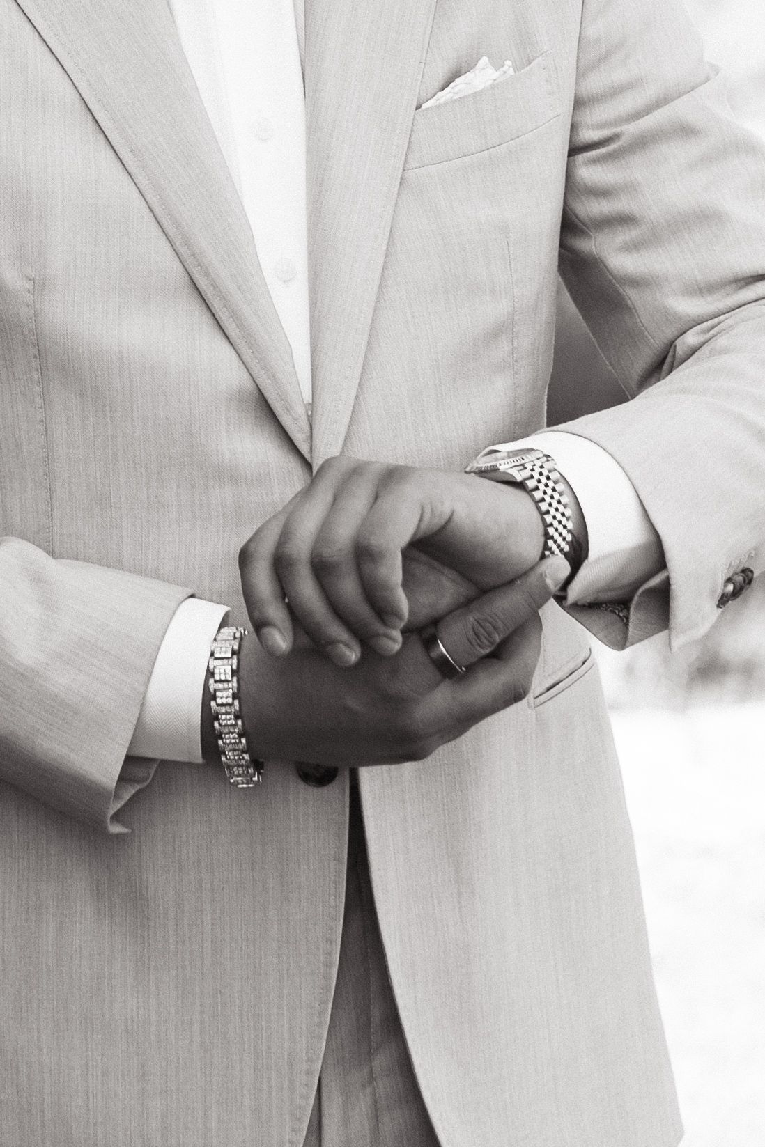 Close-up black and white photo of hands adjusting watch and cuff links while wearing a light colored suit jacket.