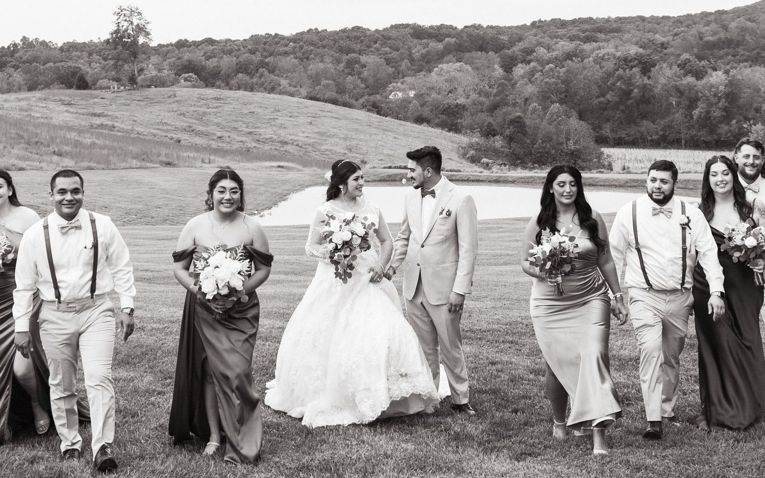 A wedding party walks together across rolling hills in black and white, with the bridal party dressed in elegant attire.