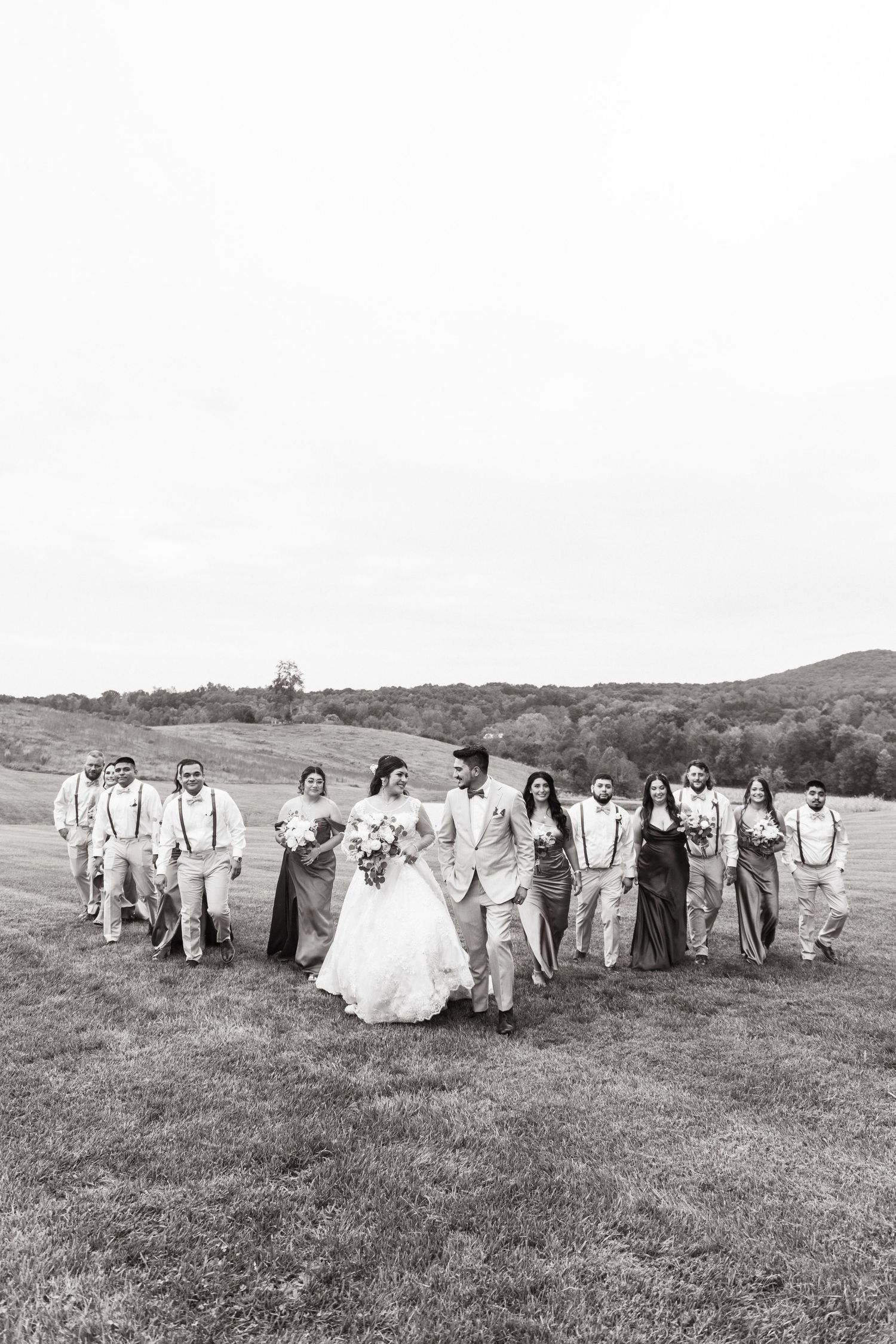A wedding party walks together through a grassy field in black and white.