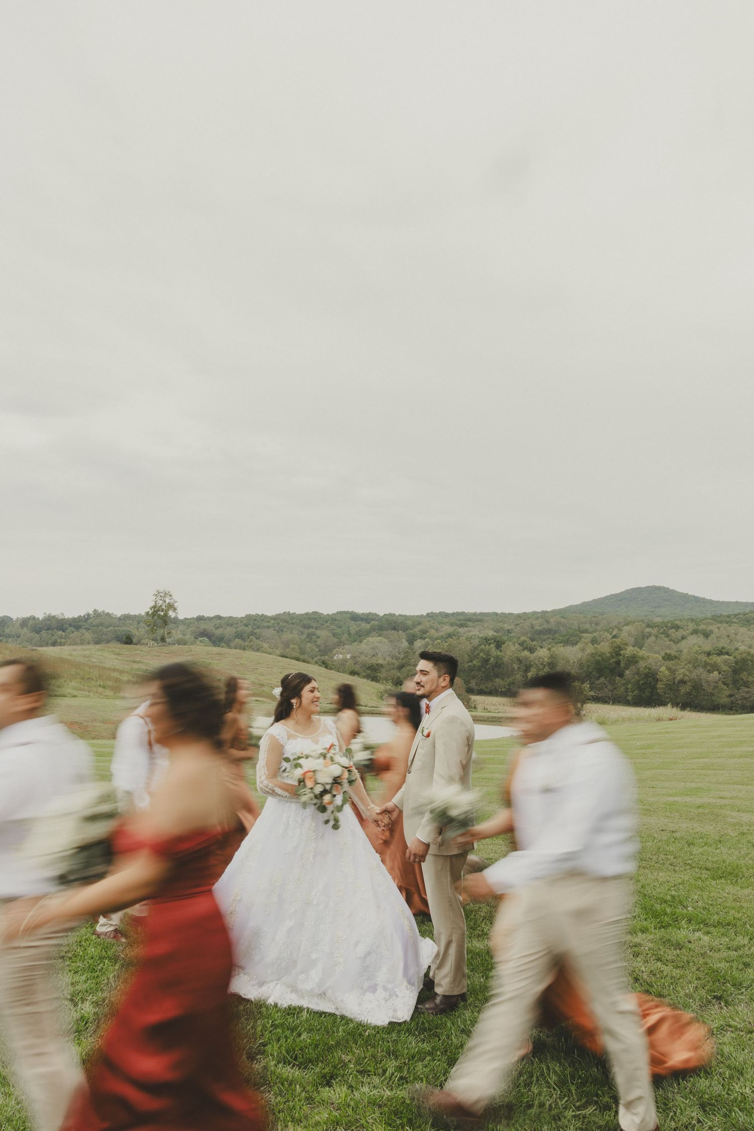 Motion-blurred wedding party on a grassy hilltop with mountains in the background showing movement and energy.