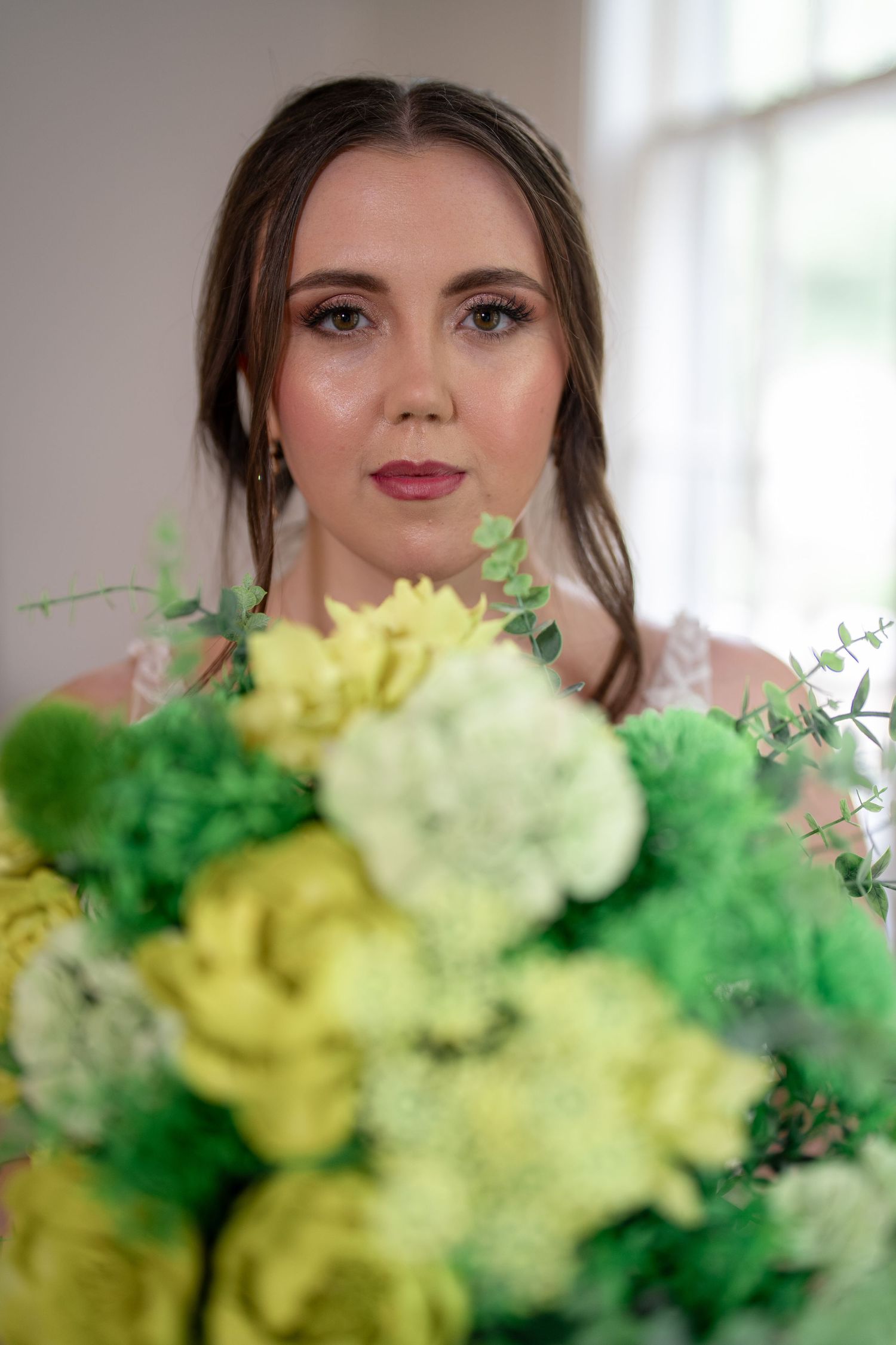 Elegant bridal portrait featuring yellow and green floral bouquet against soft white background.