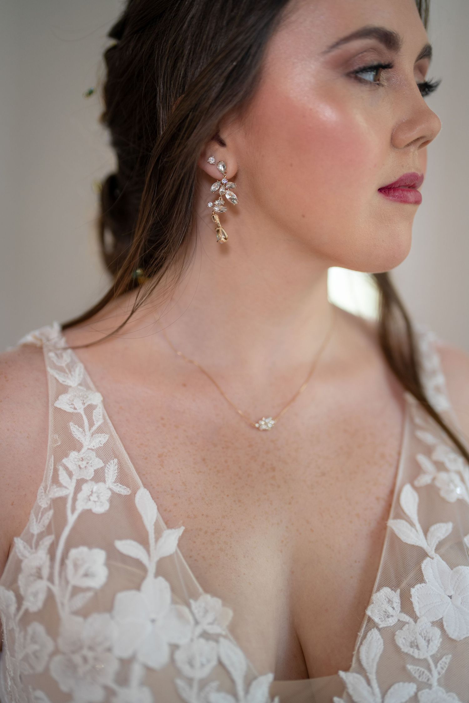 Elegant bridal details showing delicate floral lace dress neckline with crystal jewelry and earrings.