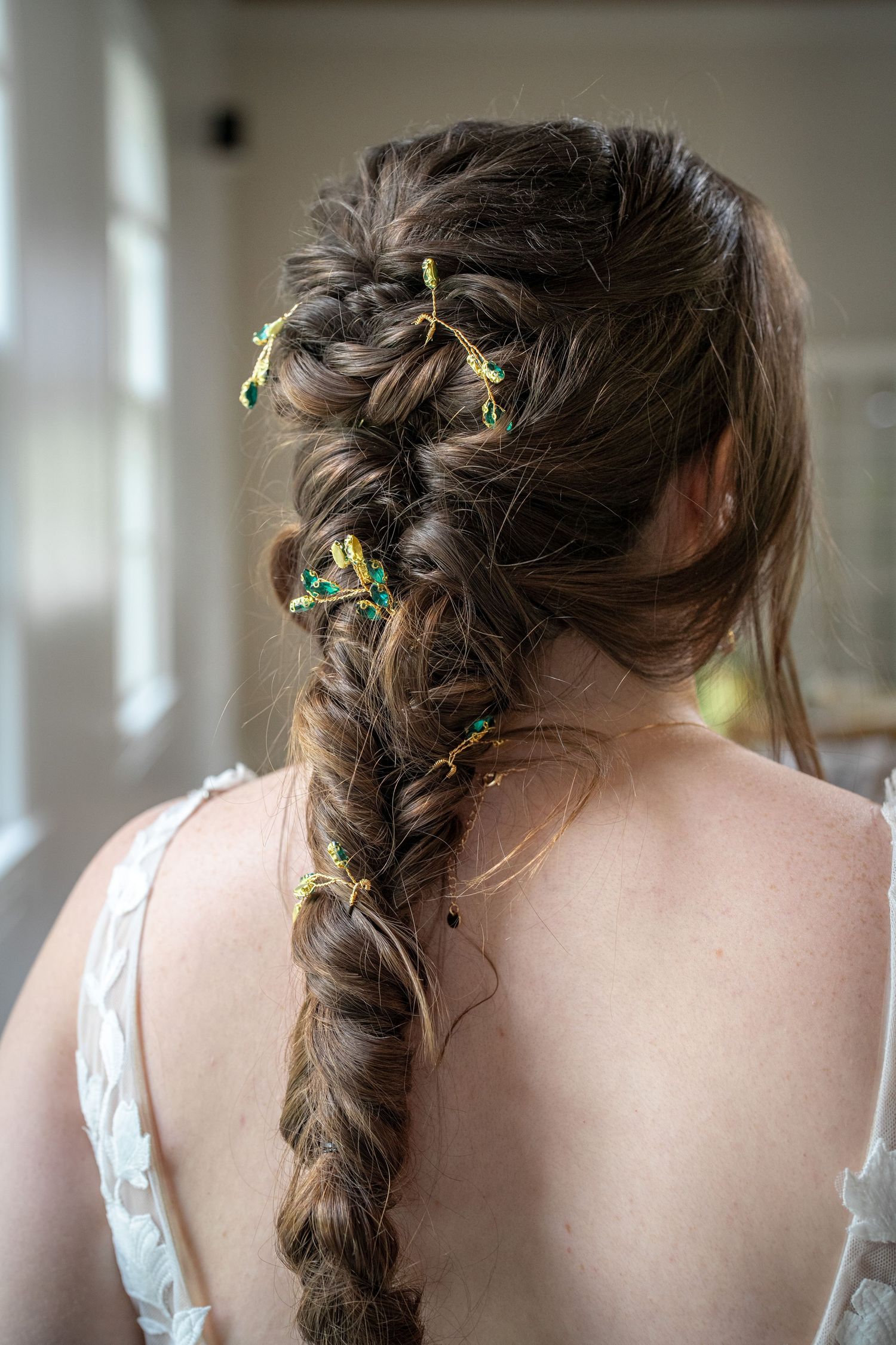 Long brown braided hairstyle adorned with small green and yellow flowers woven throughout.