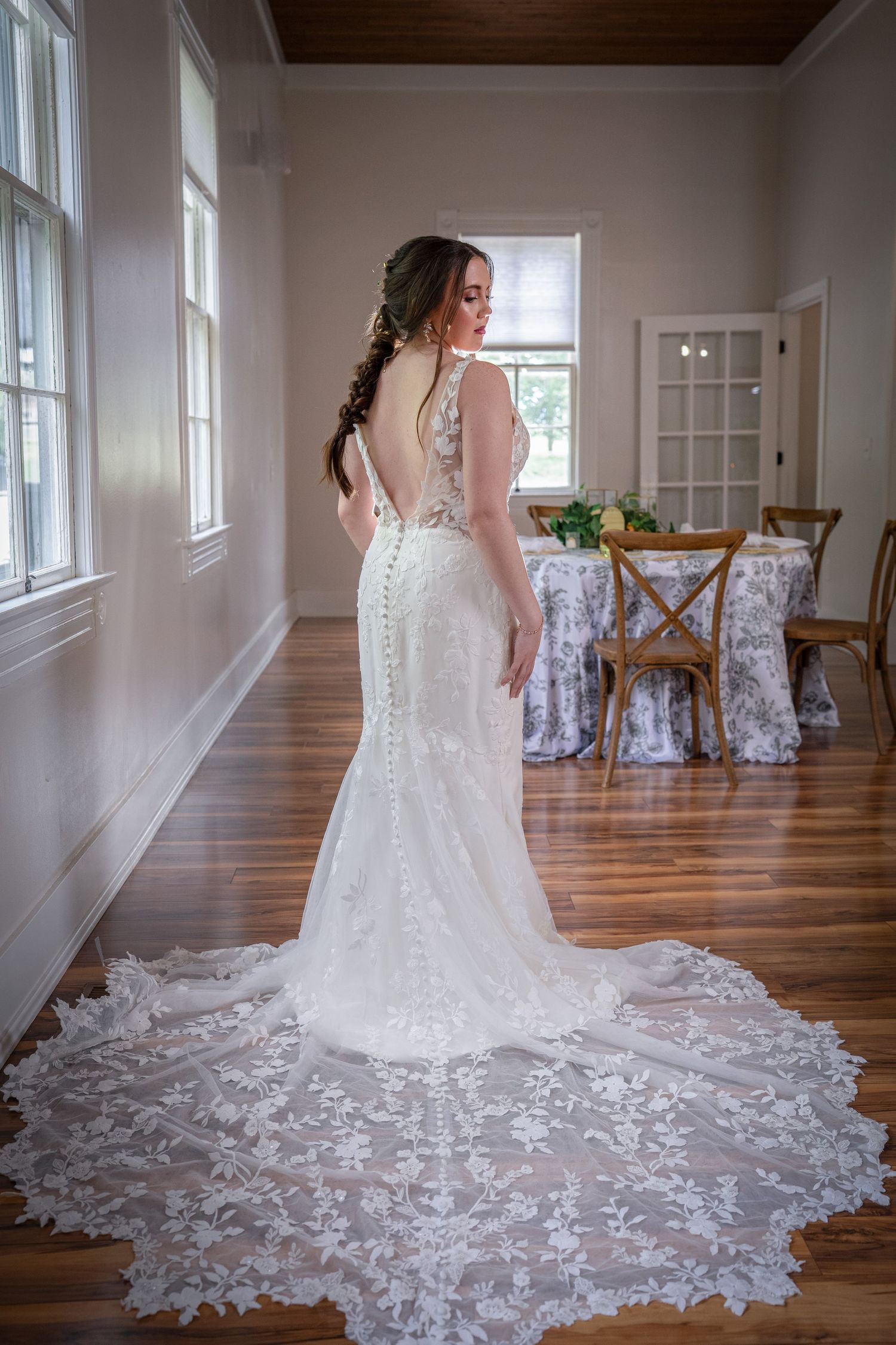 Lace wedding dress with dramatic train and button details photographed in bright natural light room.