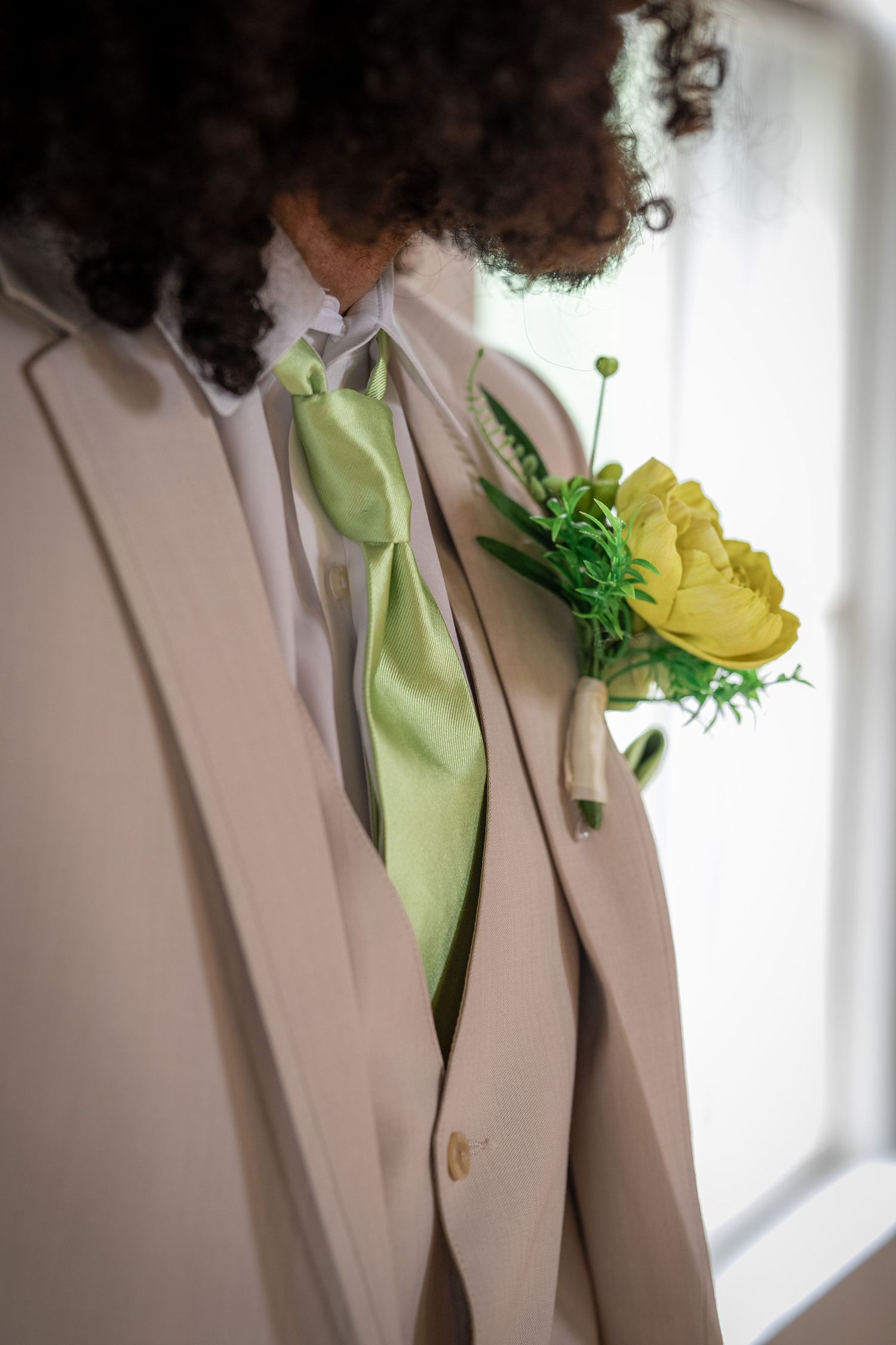 Close-up detail of a beige suit jacket with mint green tie and yellow floral boutonniere.