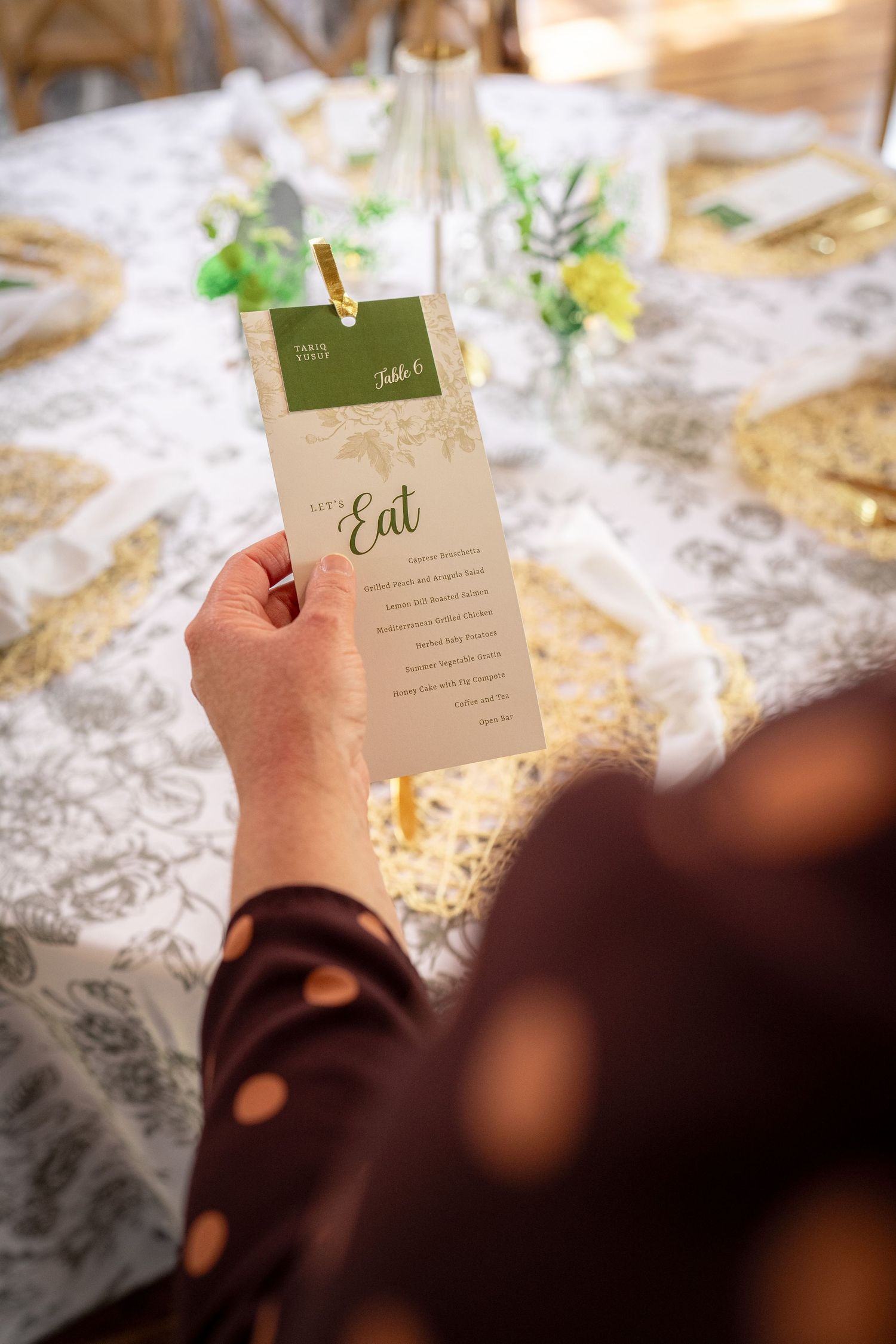 Hand holding elegant wedding menu card with 'Eat' text against white tablecloth at formal place setting.
