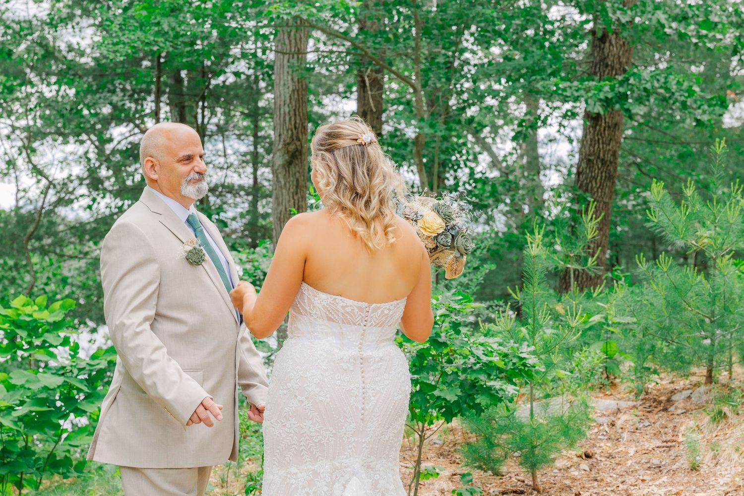 A couple shares an intimate moment during their summer wedding while standing in a lush green forest setting.