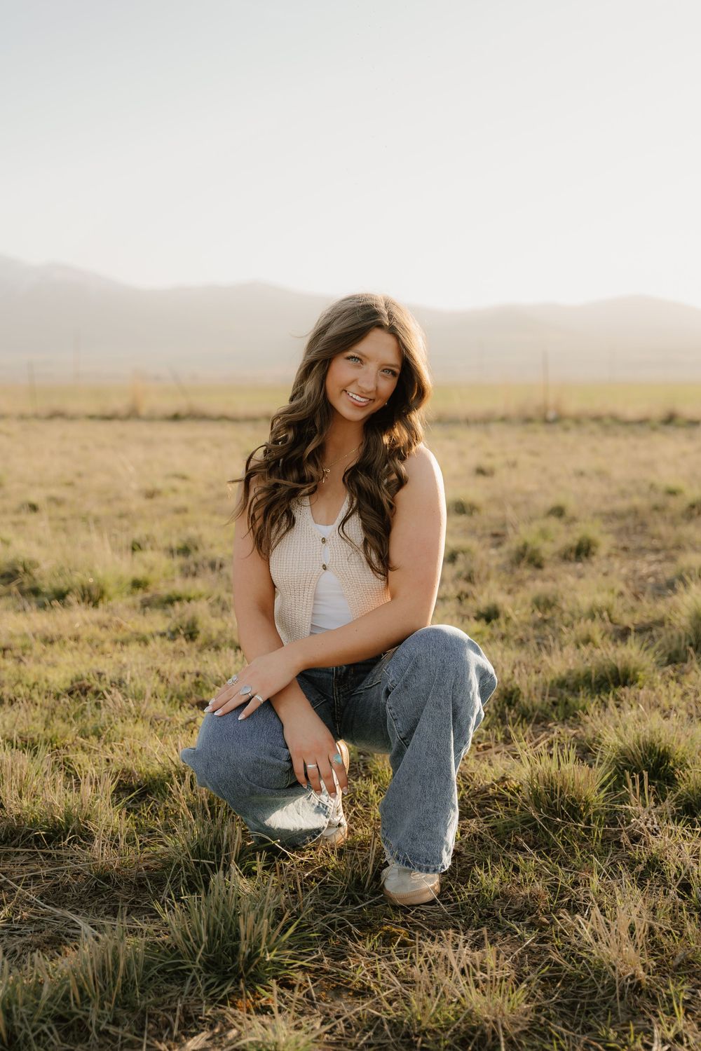 Portrait taken in golden field at sunset with mountain silhouettes in background.