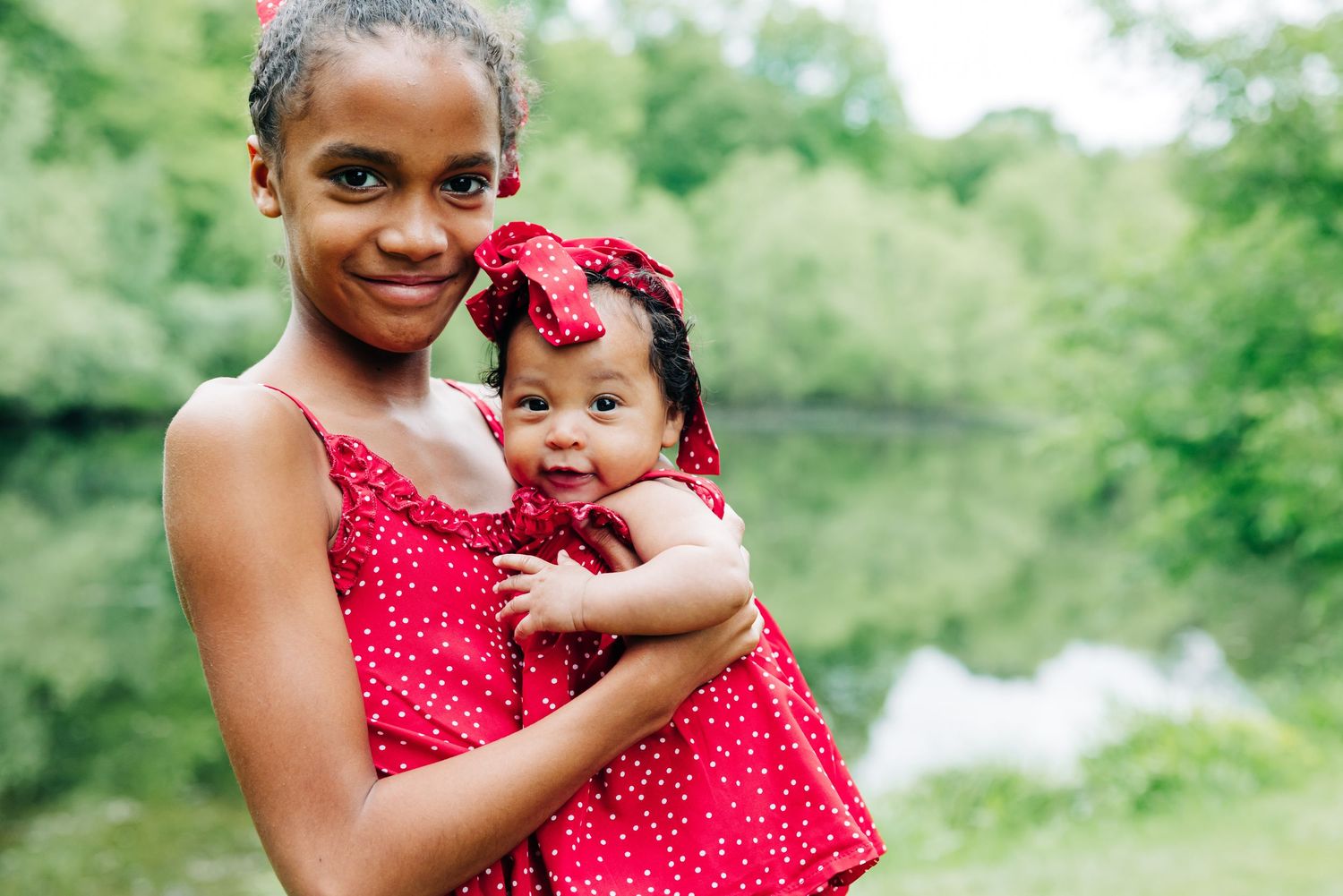 A tender moment captured between sister and baby sister wearing matching red dresses while at Brooksvale Park