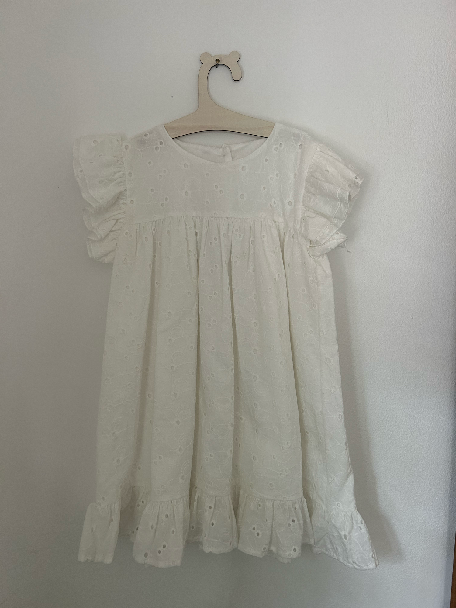 White knit baby romper with 'ONE' text and small bow detail in pink embroidery against hanging clothing background.
