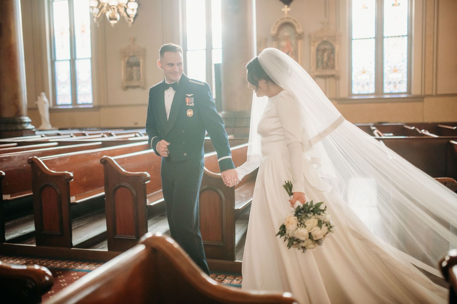 A groom leads his bride by the hand on their wedding day while walking out of the Catholic Church where they were just married.
