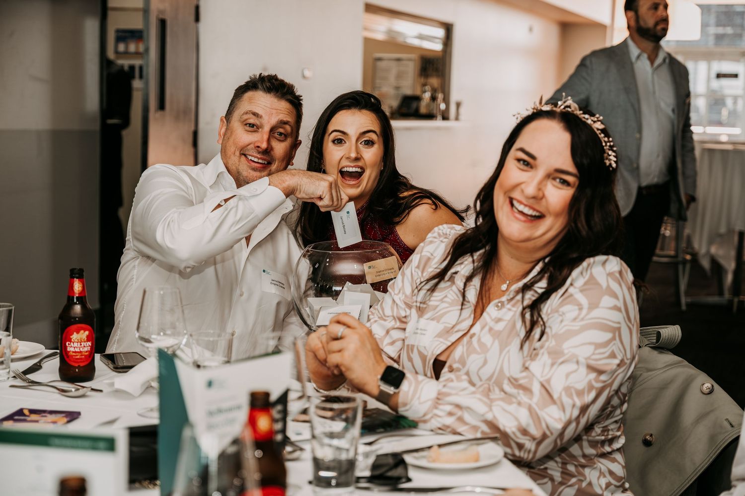 Three friends laughing and enjoying drinks together at a casual gathering in an indoor setting.