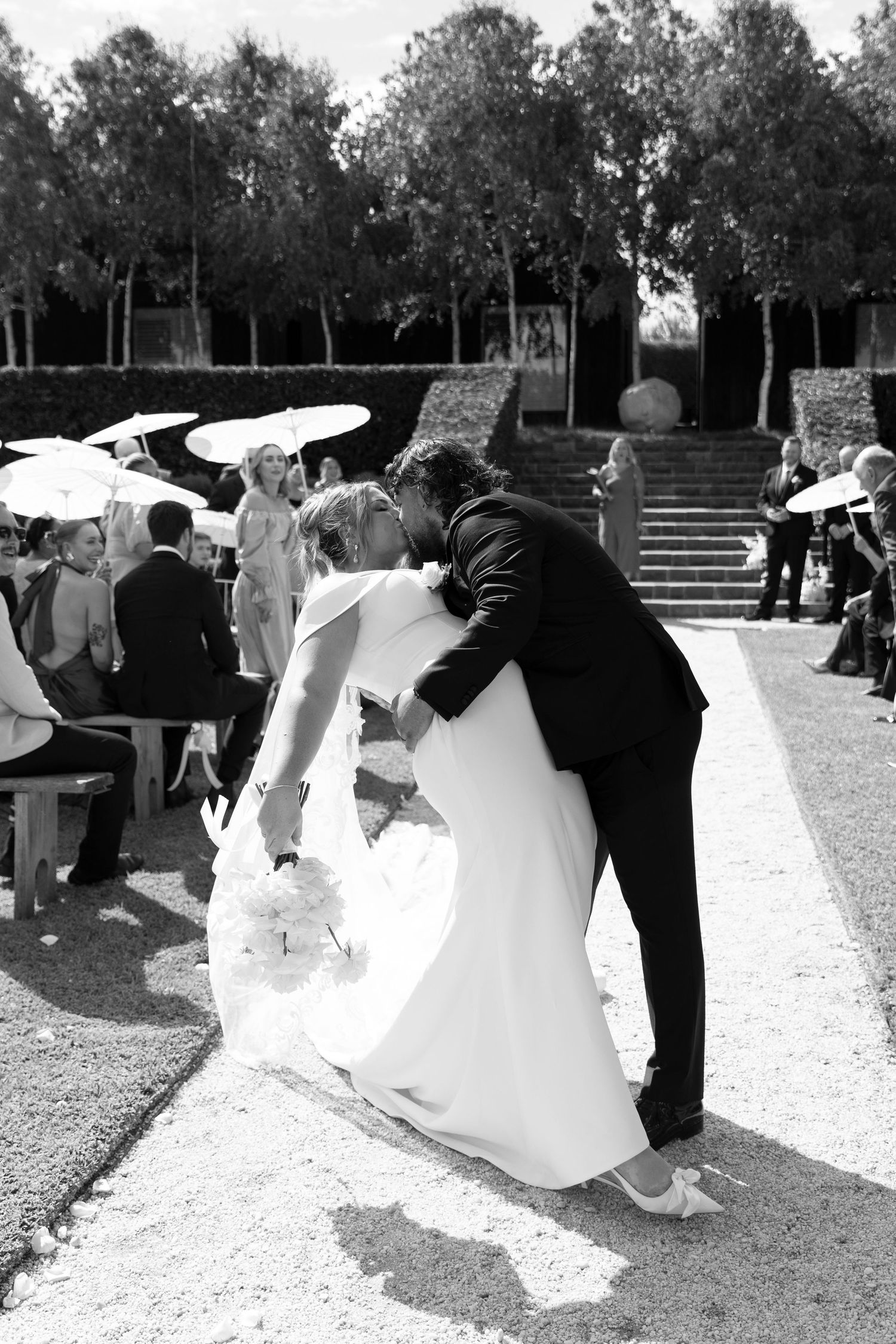 A black and white photo of a wedding celebration under umbrellas in a garden setting.