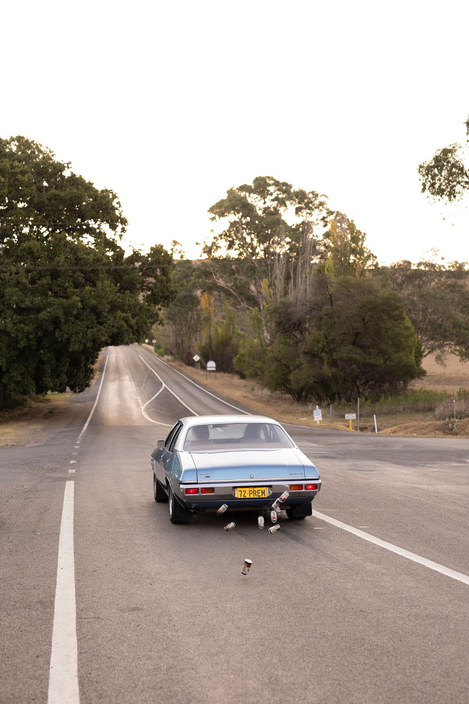Vintage blue car parked on a winding rural road surrounded by trees and natural landscape.
