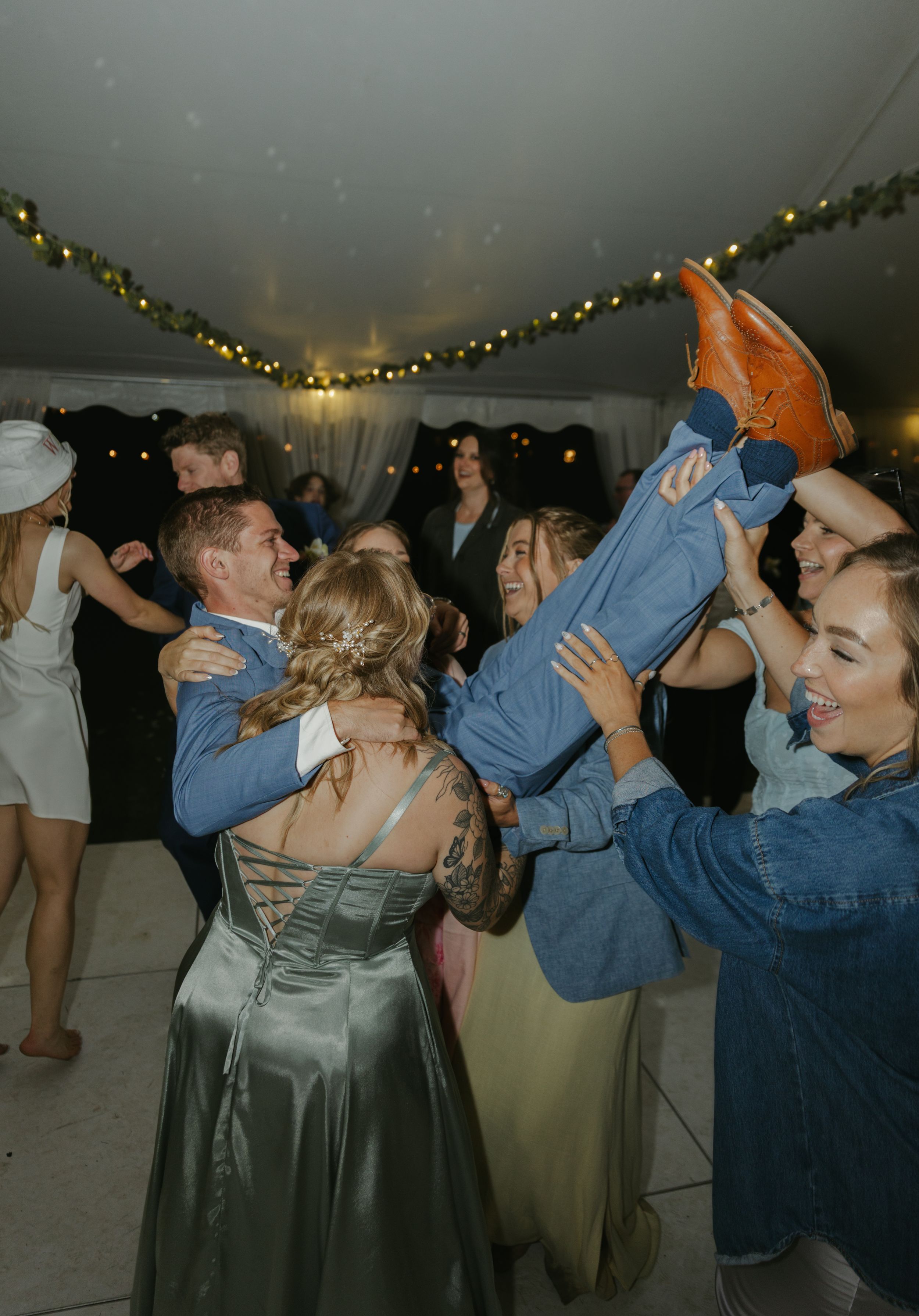 Wedding guests dance energetically under string lights at an evening reception.
