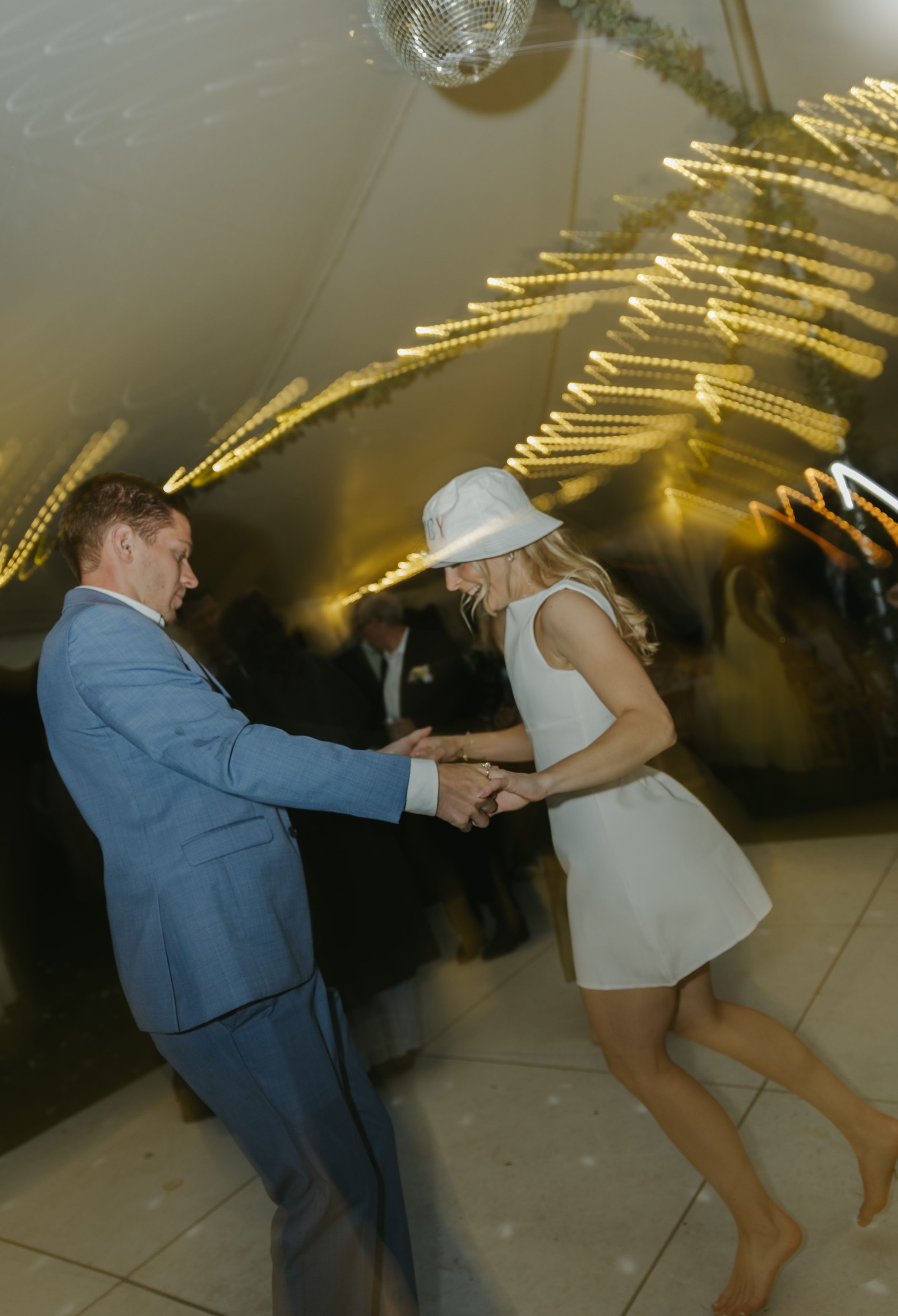 Couple shows off playful dance moves on an illuminated dance floor with golden lights above.