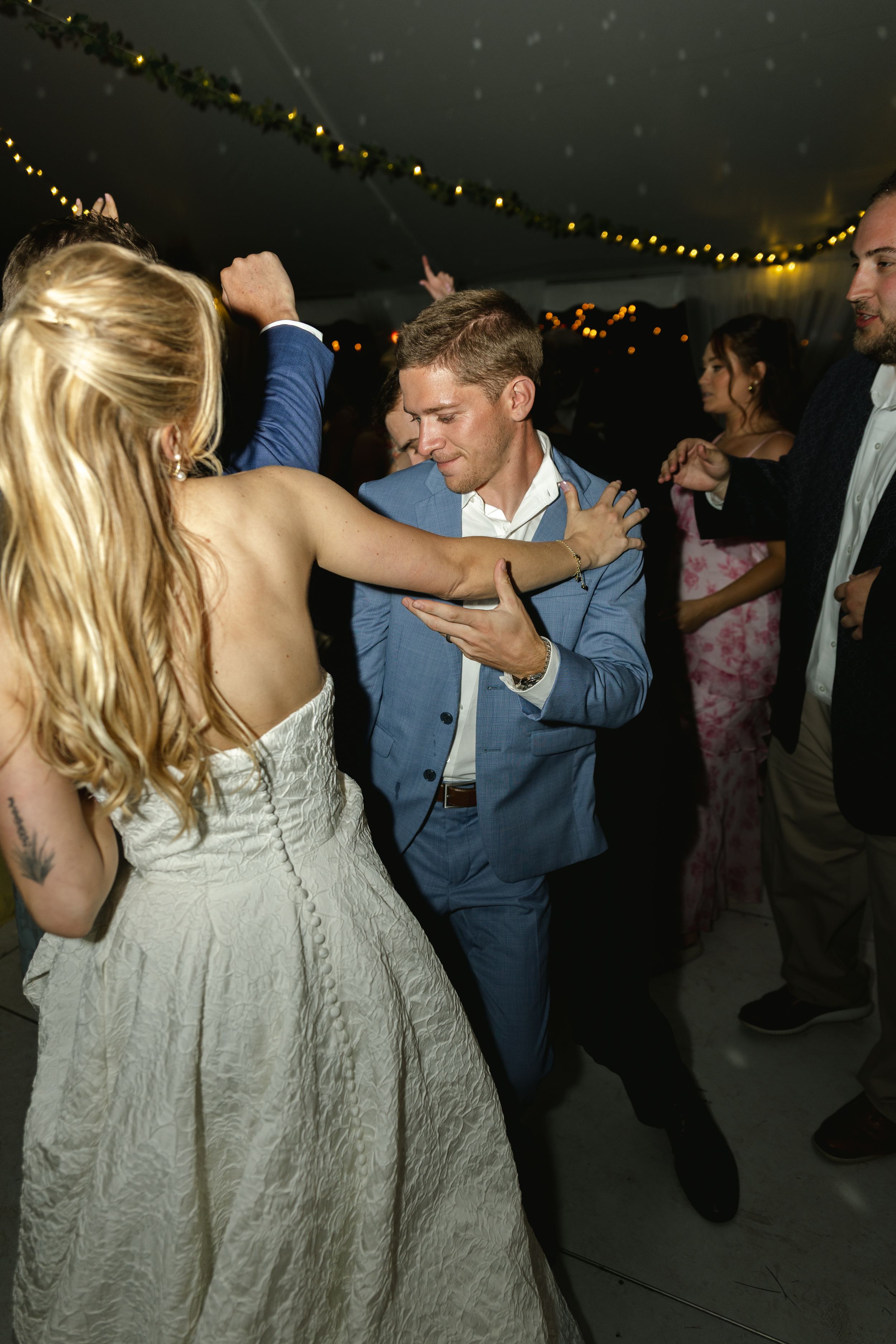 Wedding celebration with guests dancing and twirling under twinkling lights in a tent.