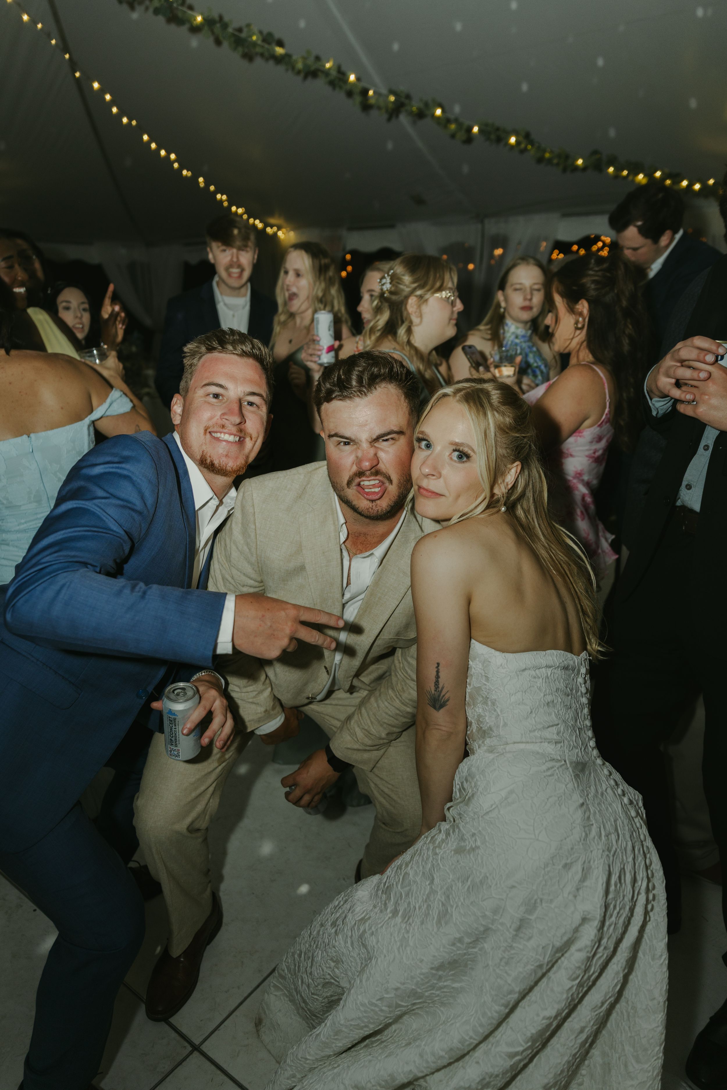 Energetic dancing and celebration at a wedding reception under string lights.