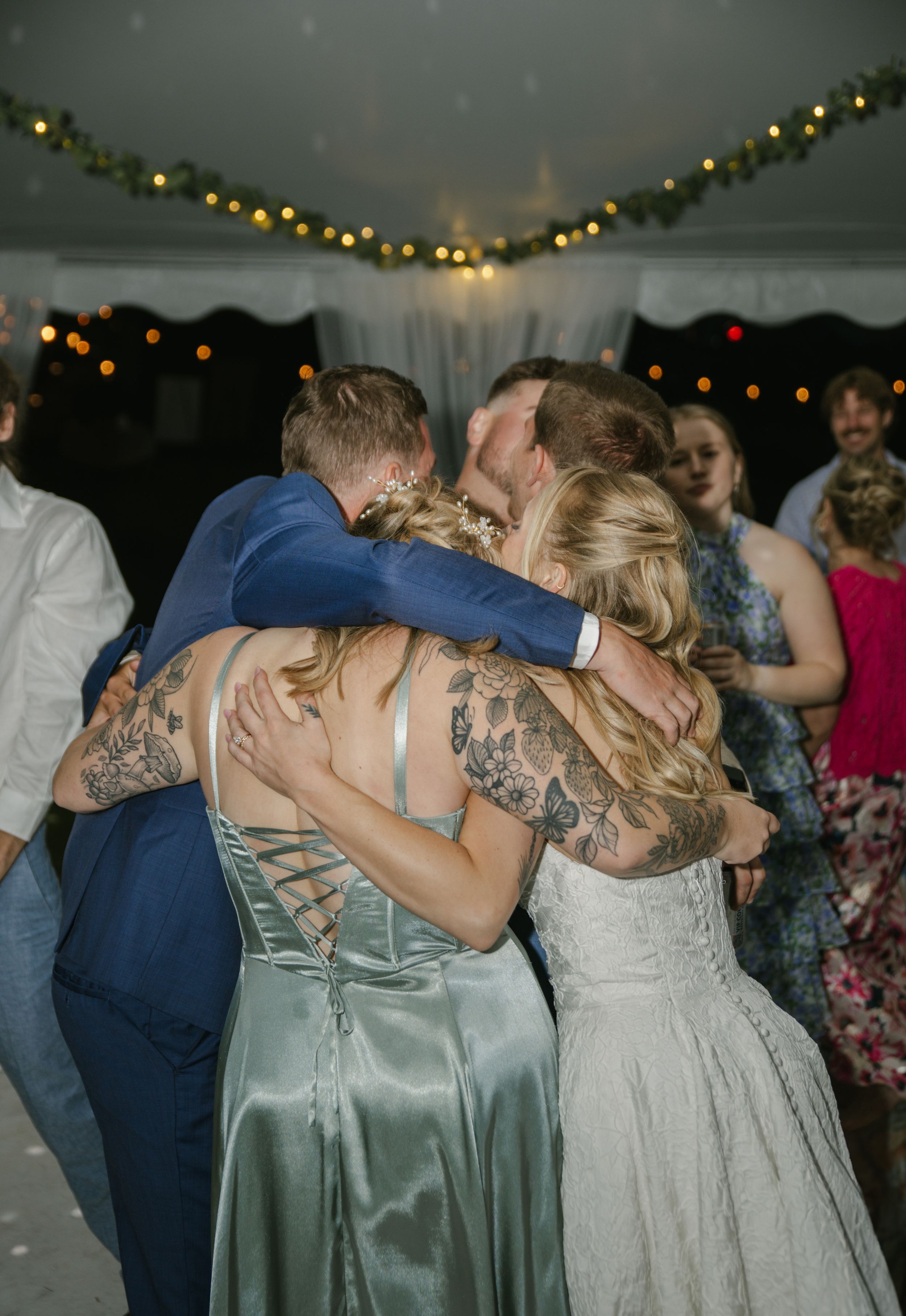 Wedding party dances together under string lights at an evening celebration.