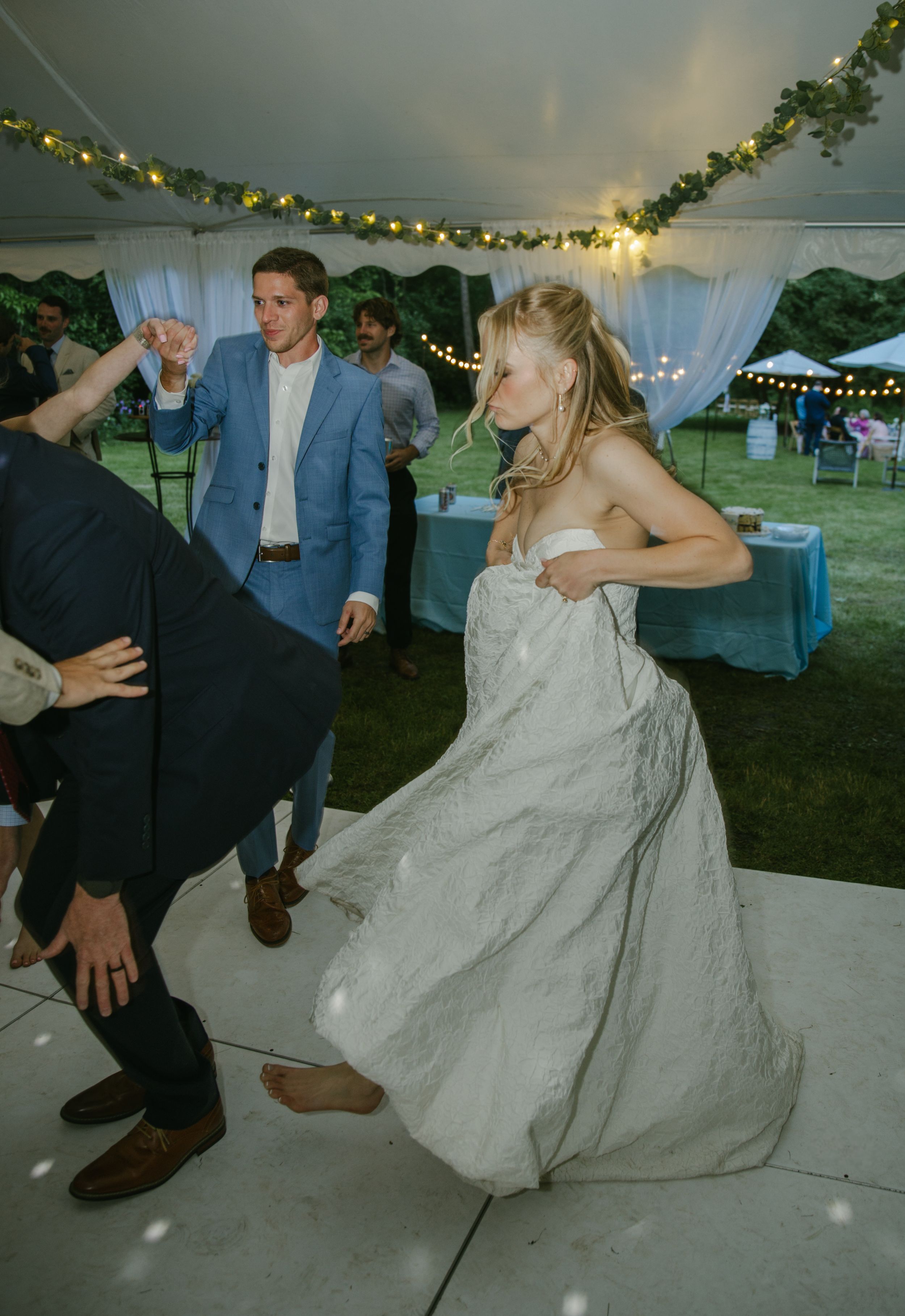 Wedding guests perform synchronized dance moves at an outdoor tented reception.