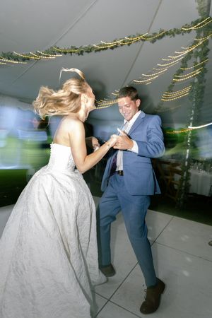A couple dances energetically under string lights and greenery at their wedding reception.