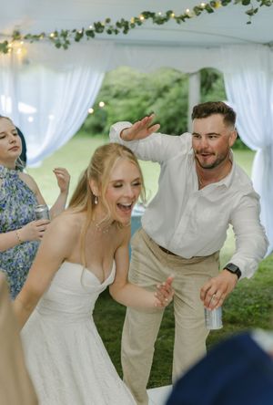 Wedding guests dancing and celebrating with joy under a white tent with fairy lights and greenery.