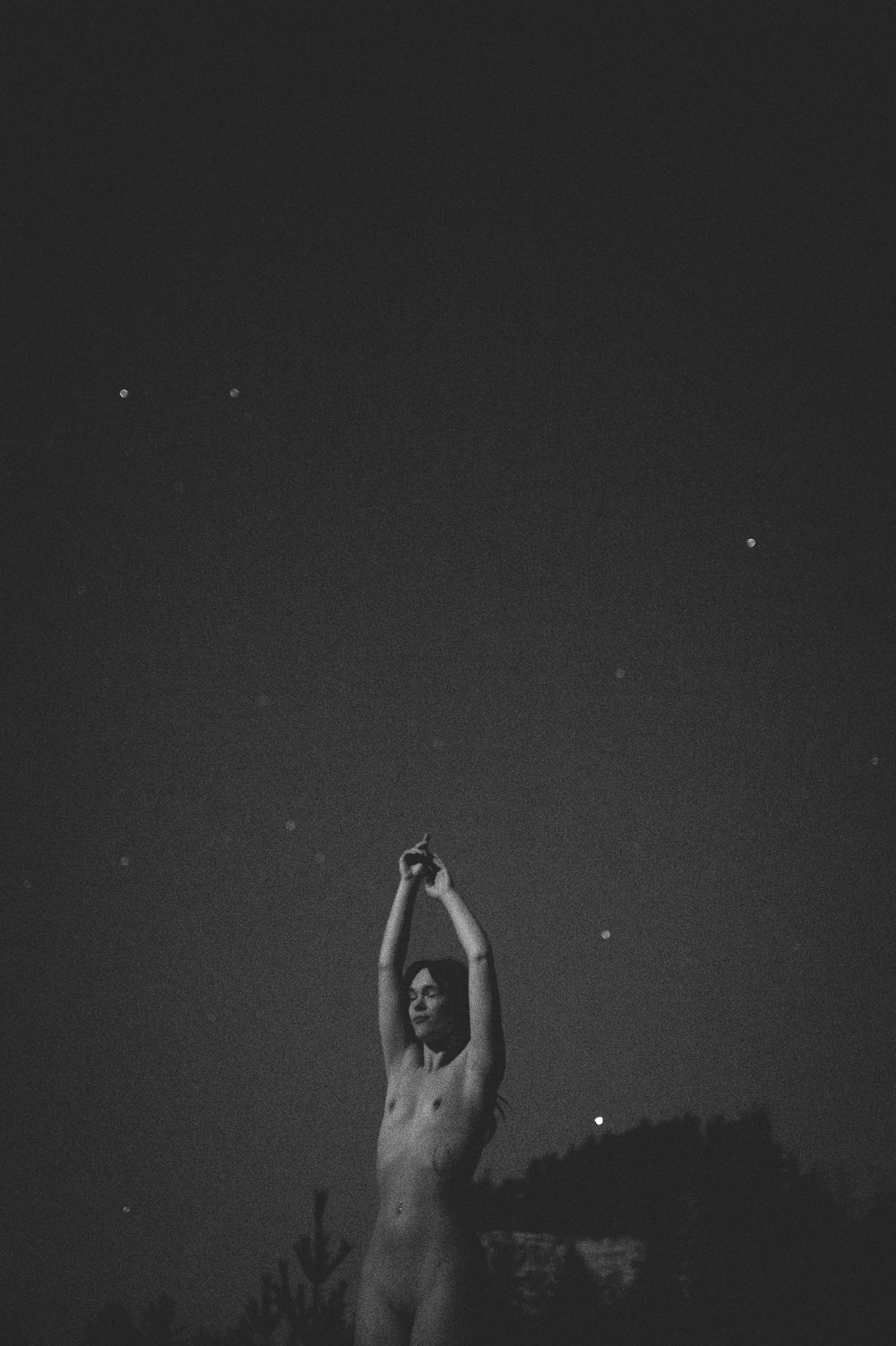 A black and white artistic photo of a silhouetted figure reaching up toward the night sky with stars visible.