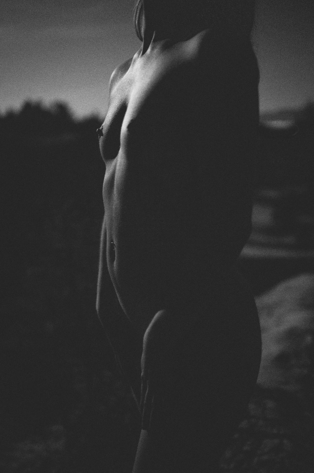 Low key black and white artistic nude figure study highlighting shadows and curves against a dark background.