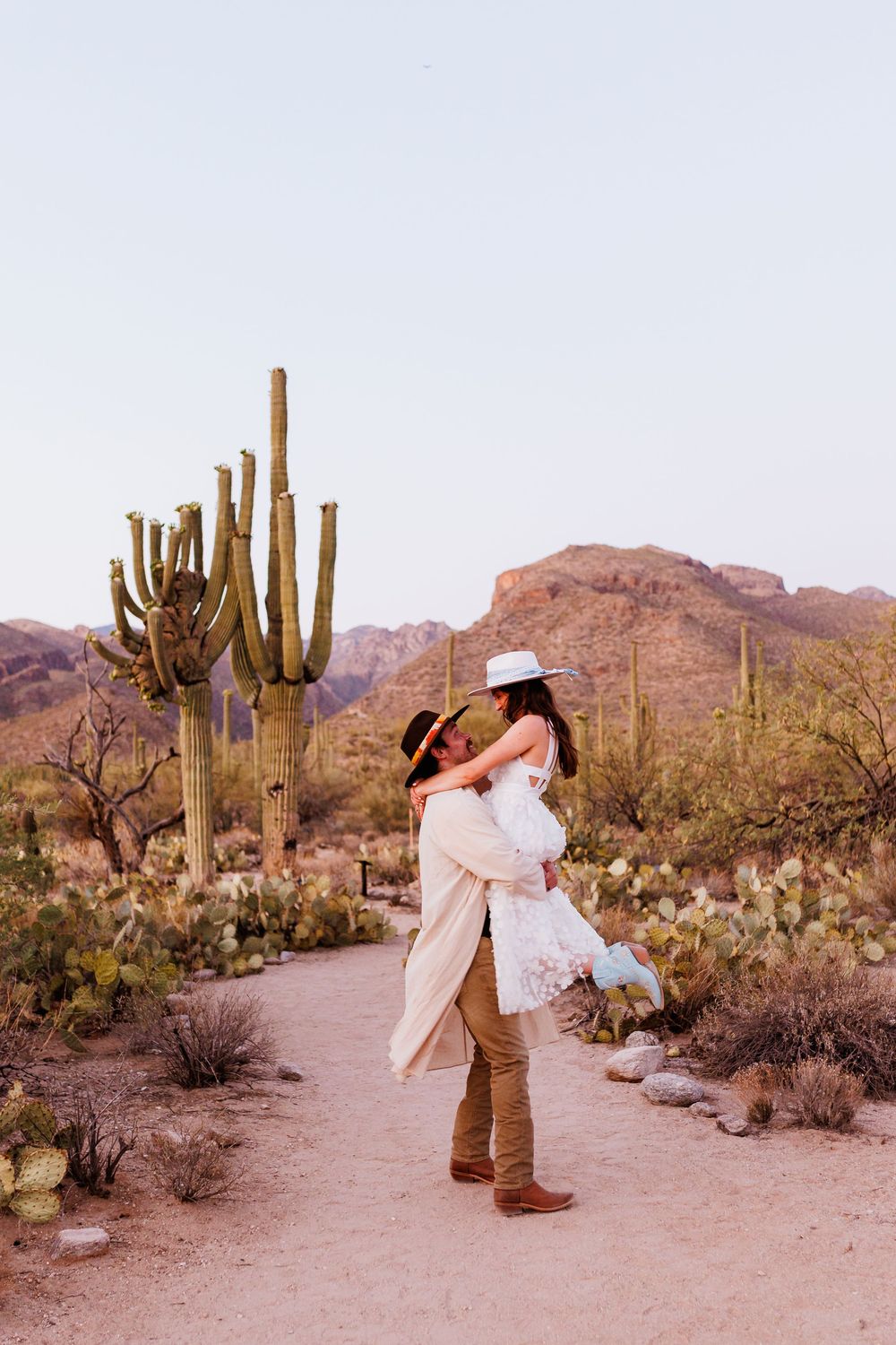 Desert engagement photoshoot in Saguaro National Park with majestic saguaro cacti and mountains in background at sunset.