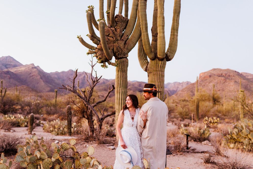 A series of desert engagement photos featuring a couple amongst towering saguaro cacti and rugged mountains at sunset.