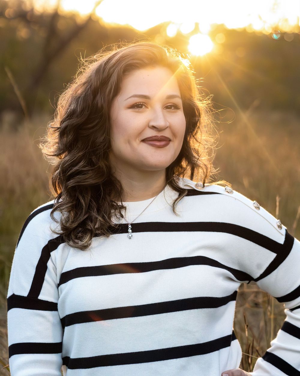 Portrait photo outdoors with golden sunlight against a natural background wearing a black and white striped sweater.