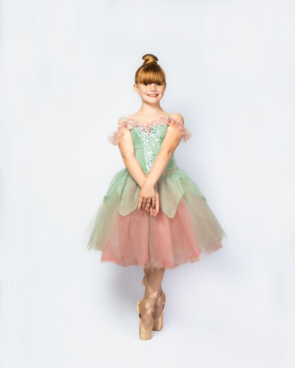 Young ballerina in green and pink tutu dress poses en pointe for a professional dance portrait photo.