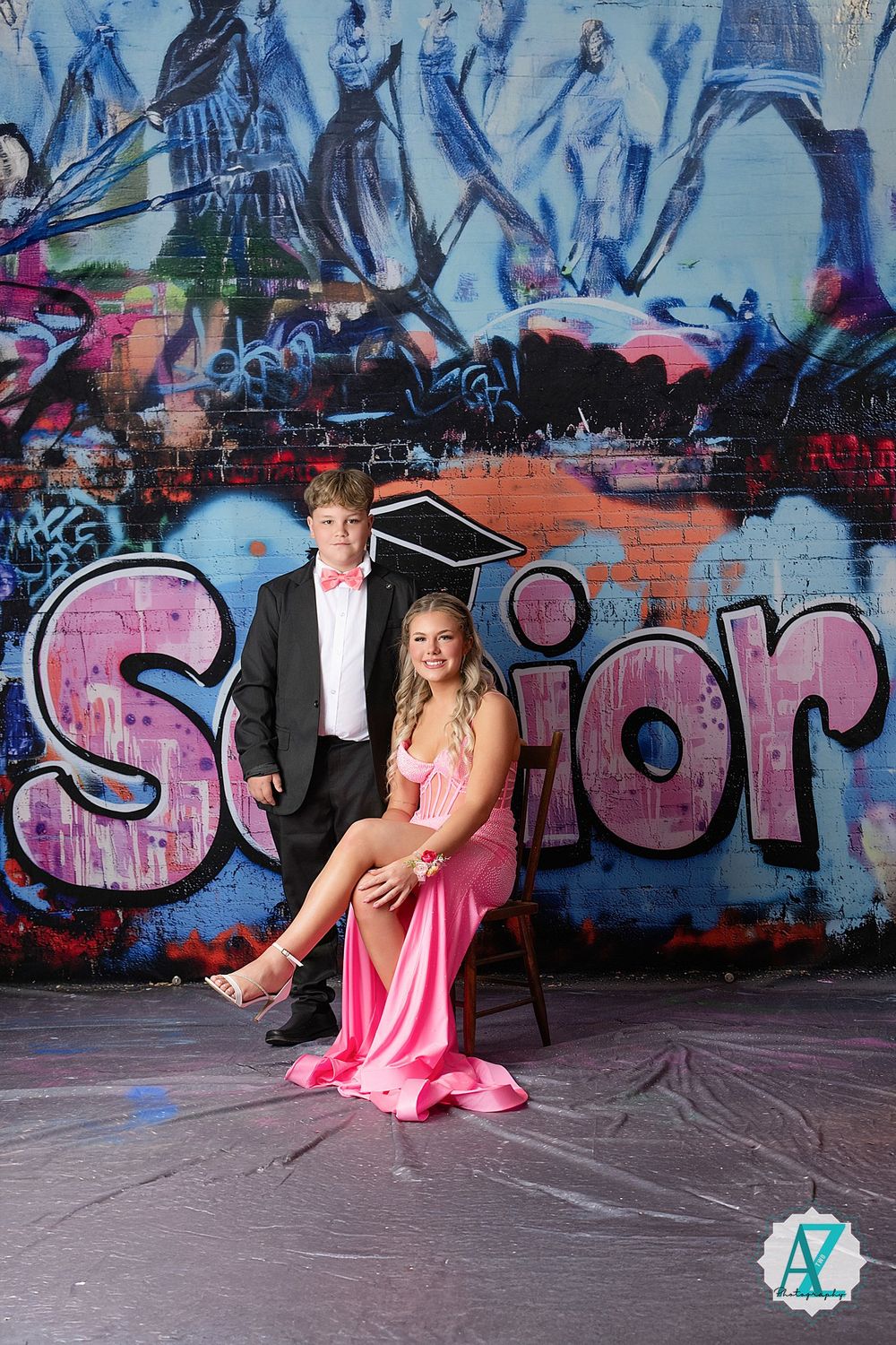 Formal couple poses in front of colorful graffiti wall with pink 'Senior' text and urban artwork in background.