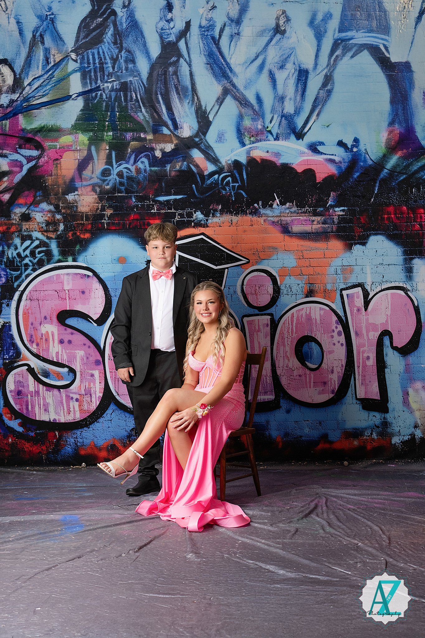 Formal couple poses in front of colorful graffiti wall with pink 'Senior' text and urban artwork in background.