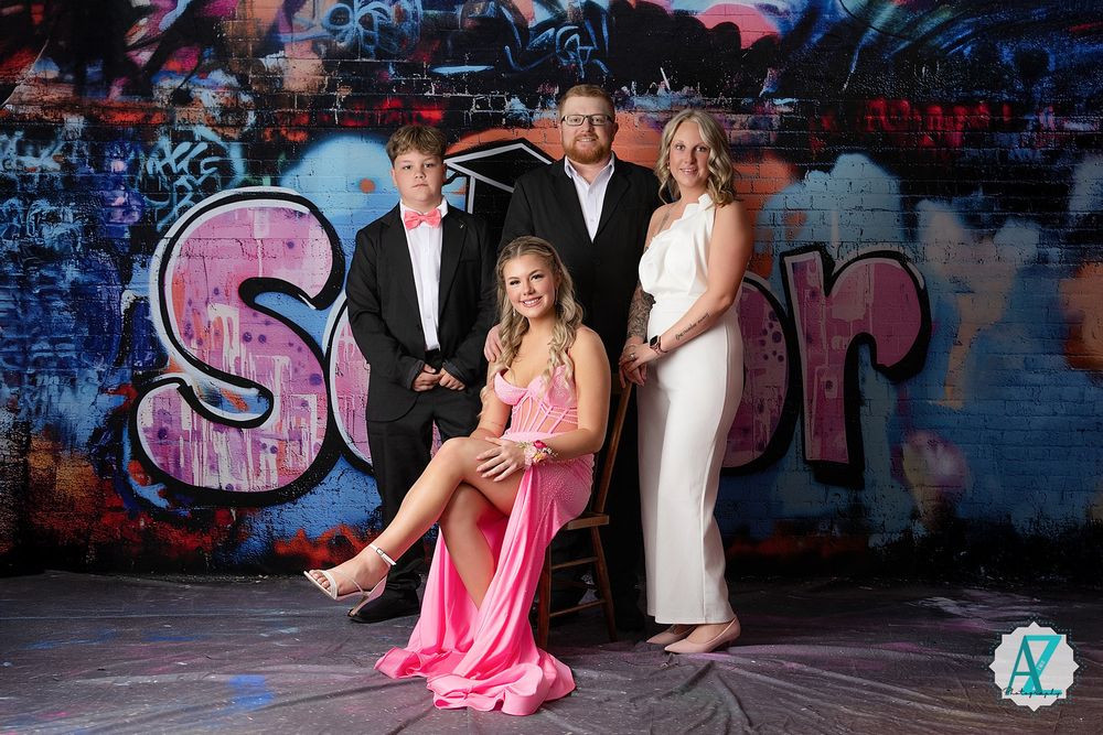 Formal group photo against graffiti wall featuring pink dress and formal attire in urban setting.
