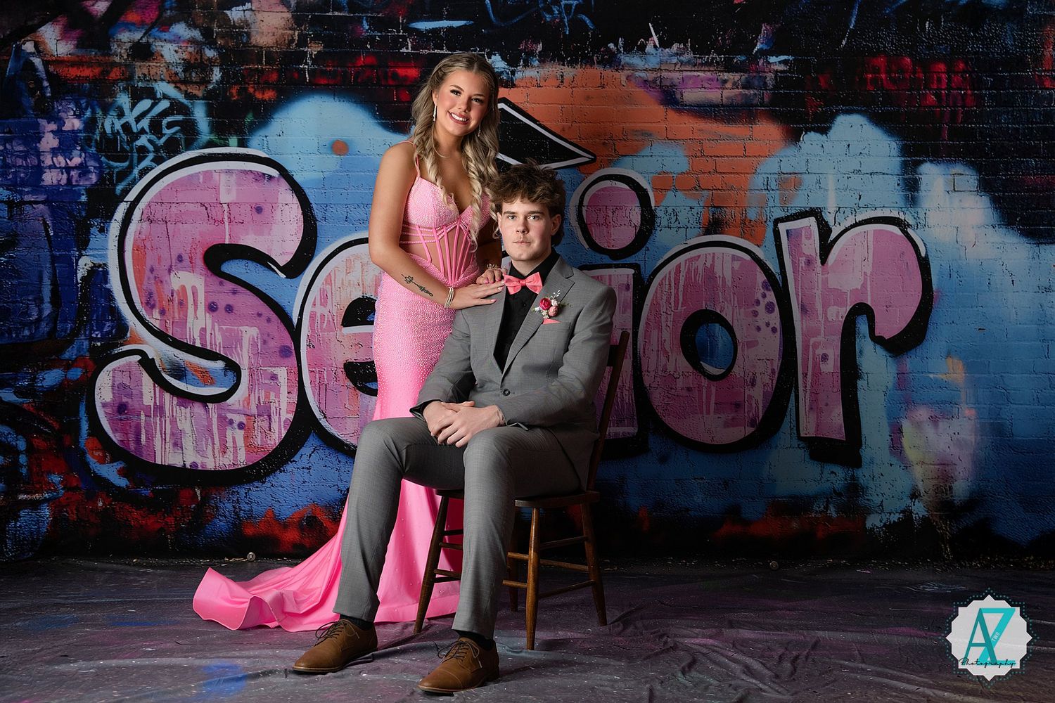 Couple poses for portrait against urban graffiti wall featuring pink dress and grey suit.