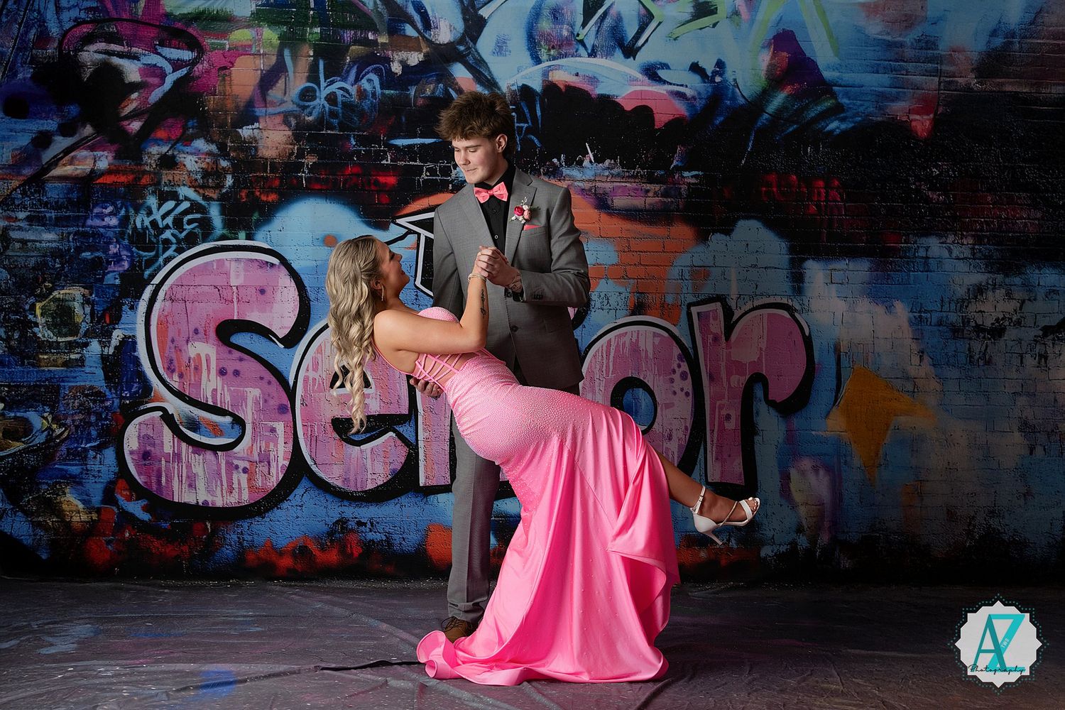 A senior portrait against a colorful graffiti wall featuring a pink flowing dress and dramatic pose.