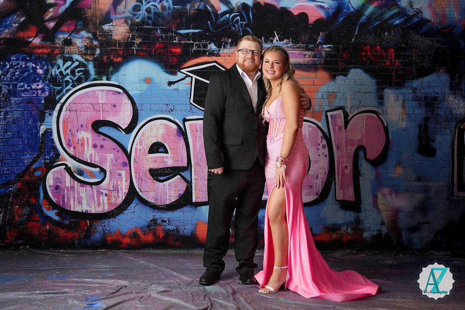 A couple poses in formal attire against a vibrant graffiti wall with pink and blue spray paint art.