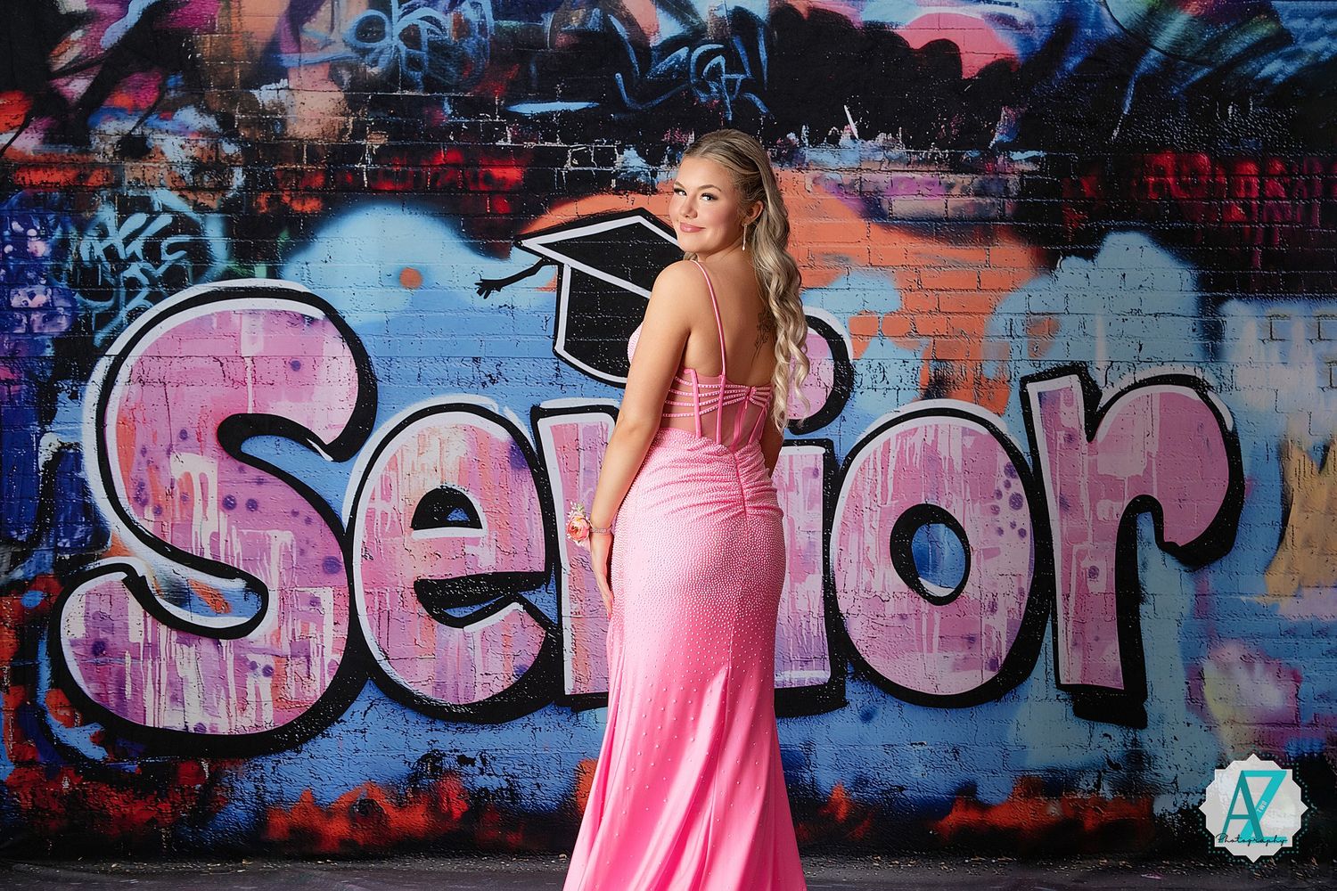 A pink formal gown worn in front of a graffiti wall featuring colorful street art and text designs.