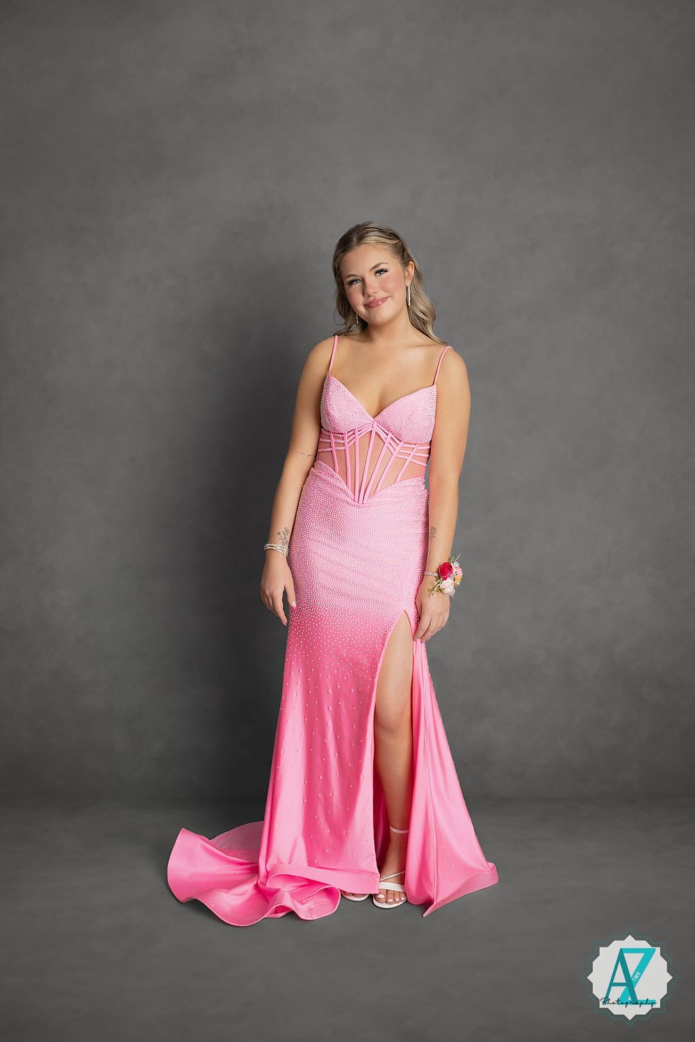 Woman in elegant pink satin formal gown with sweetheart neckline and thigh slit poses against gray backdrop.