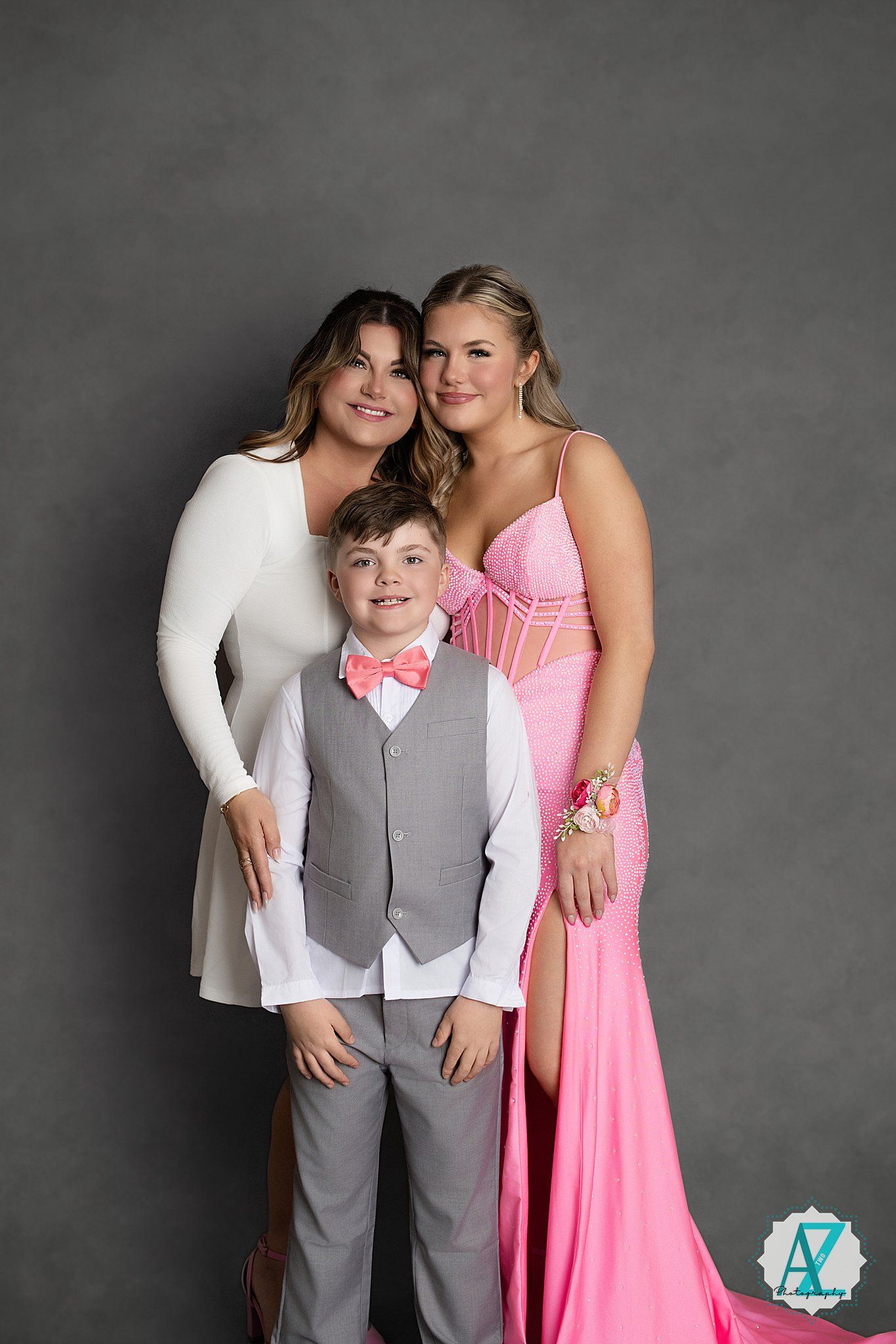 Studio portrait of three people posing together against a grey background wearing formal attire.