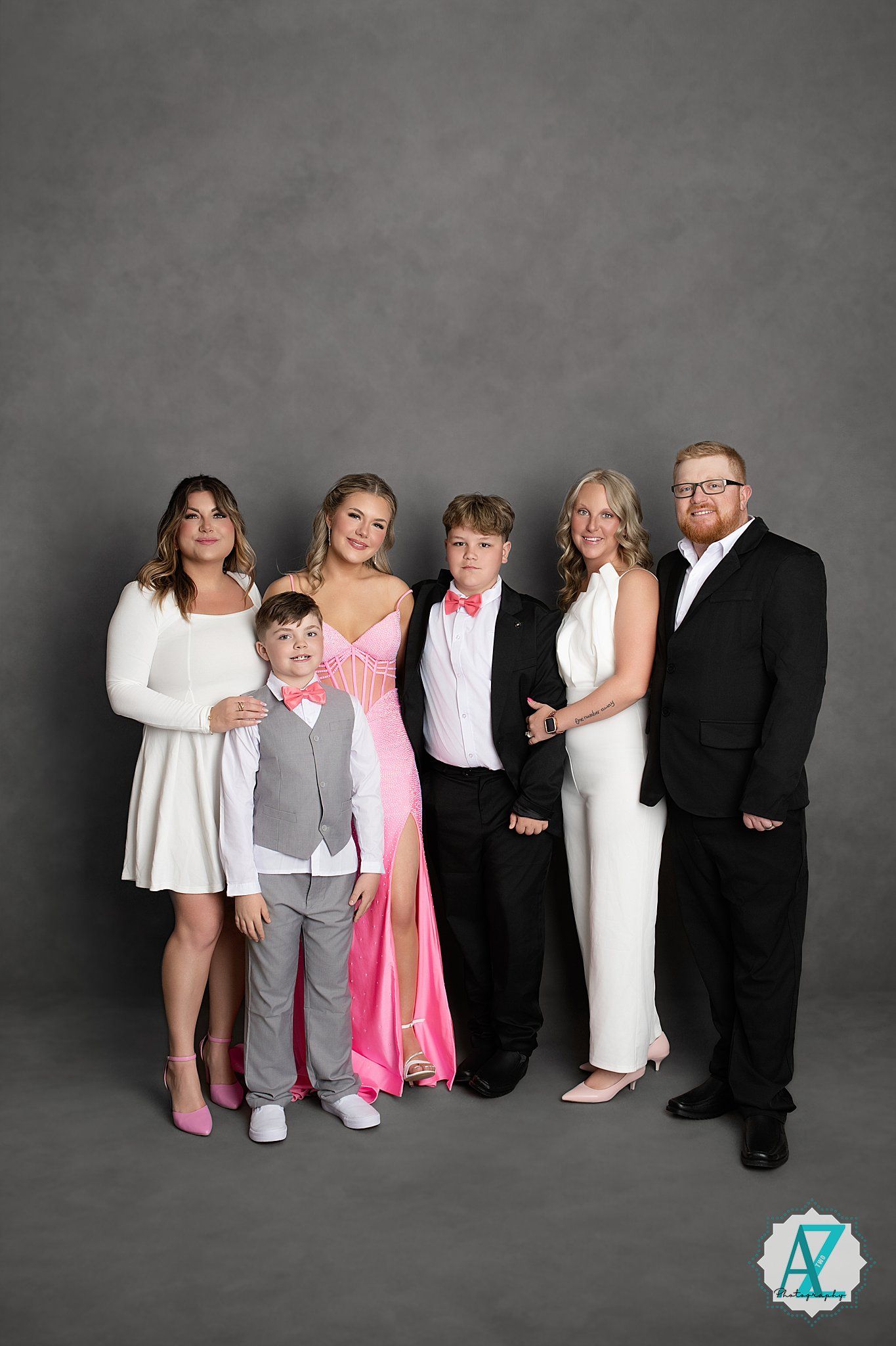 Group photo against grey backdrop showing formal attire with pink and white dresses and black suits.