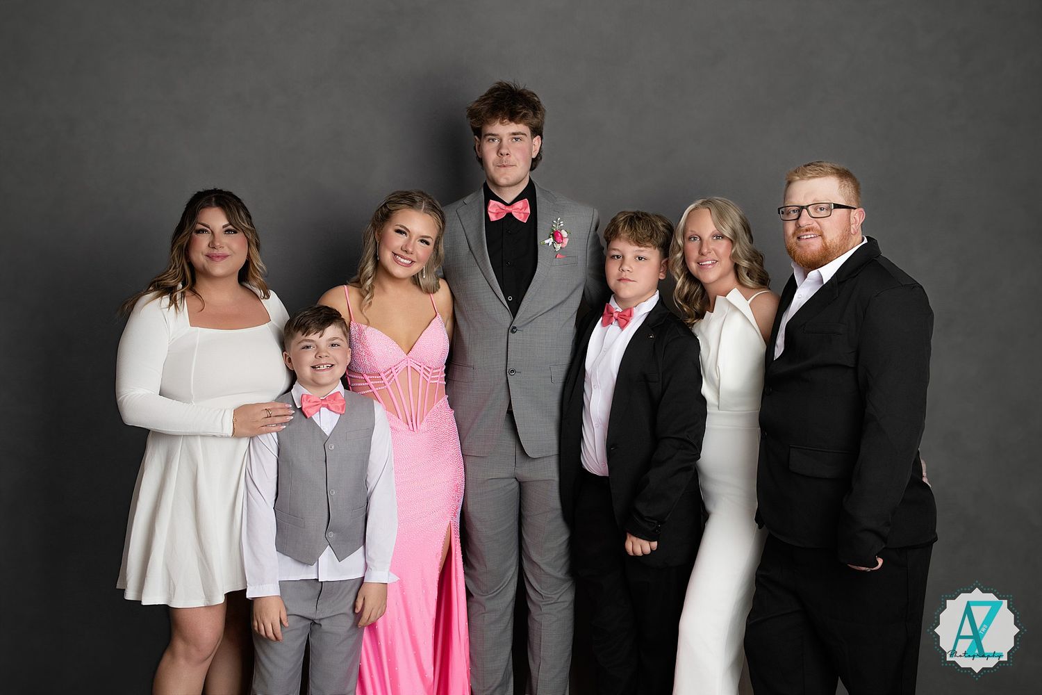 A formal family group portrait with seven people in dressy attire against a gray studio background.