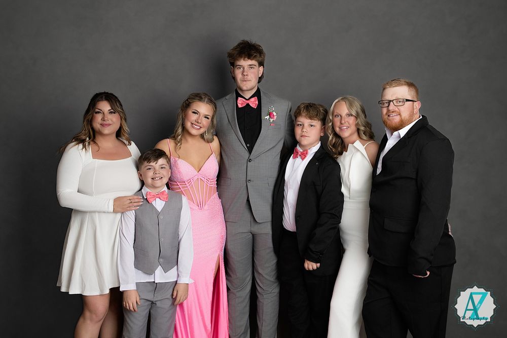 A formal family group portrait with seven people in dressy attire against a gray studio background.