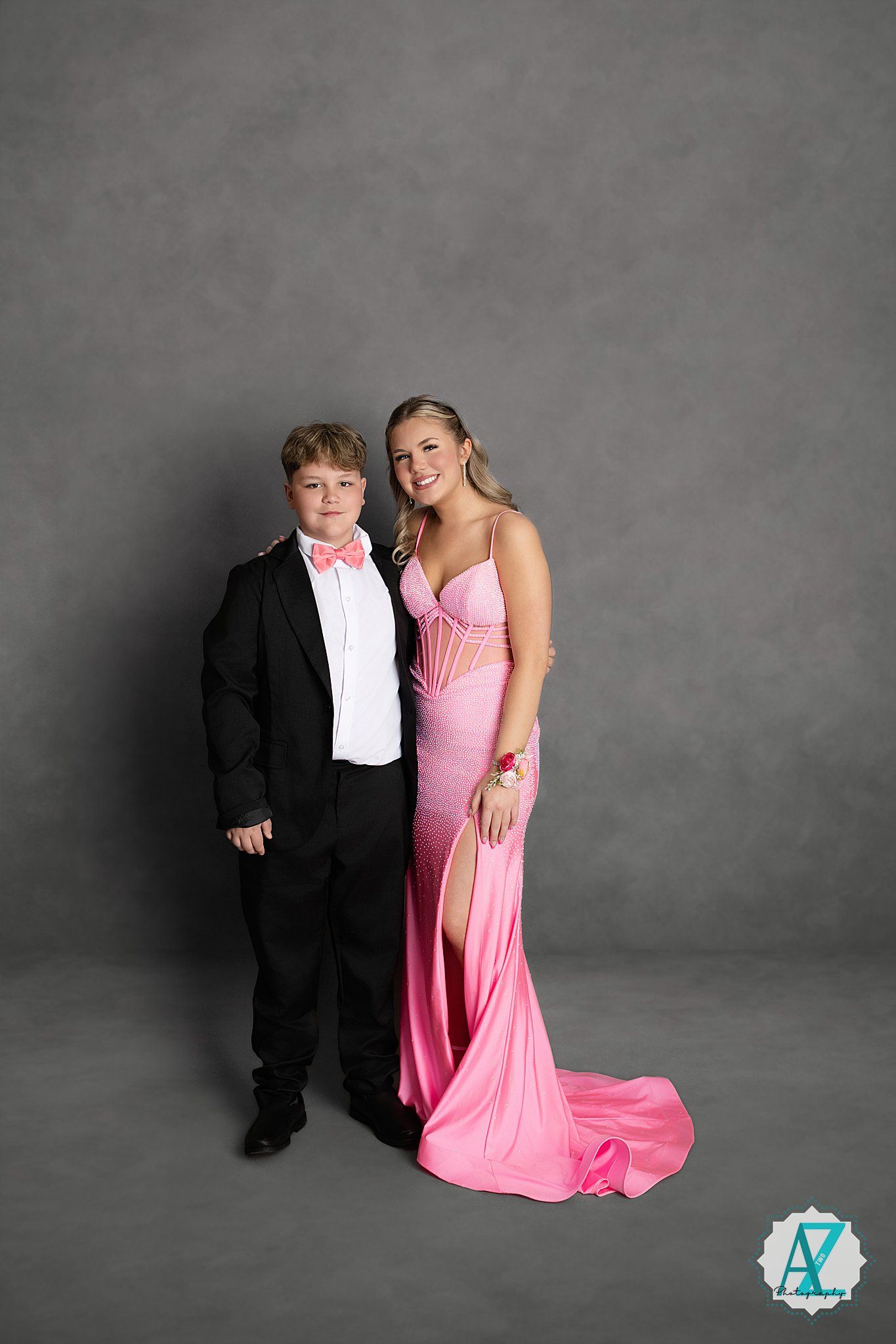 A formal portrait of two people posing together, one in a black tuxedo and one in a flowing pink evening gown.