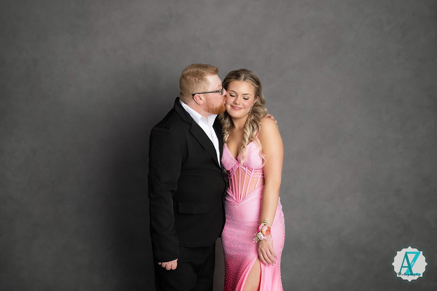 A couple in formal attire poses together against a gray backdrop at an elegant photo session.