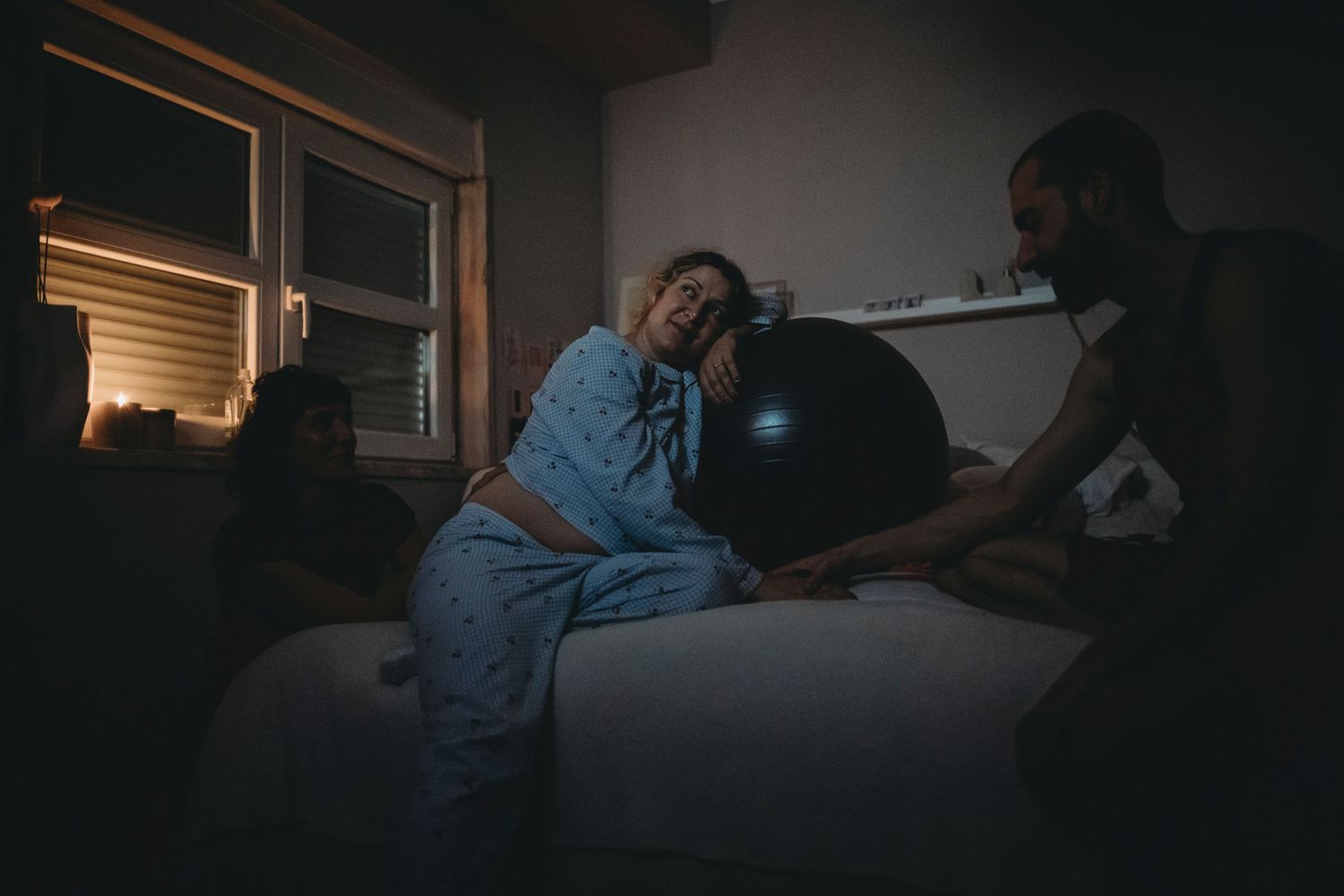 mulher gravida recebe carinho encostada na bola de pilates em cima da cama durante contração em Parto domiciliar em Lisboa