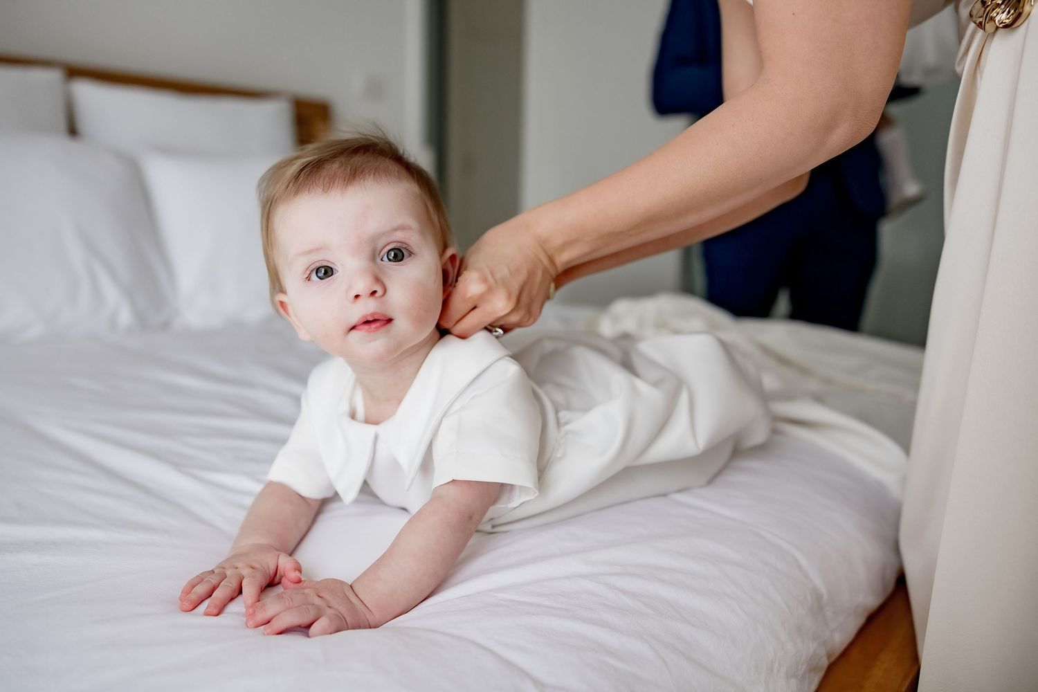 A caregiver's hand gently massages a baby laying on white bedding during a relaxing massage session.